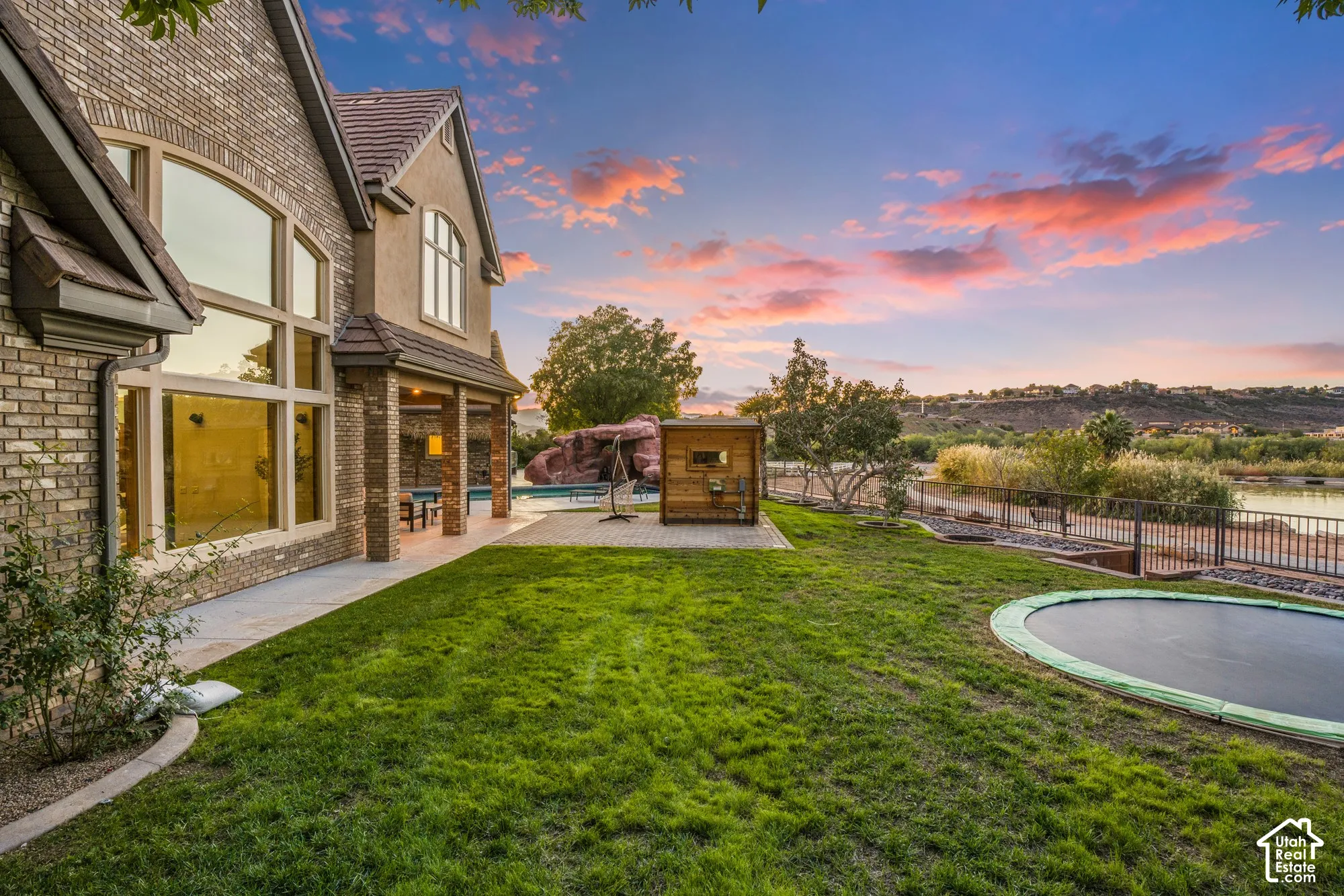 Exterior featuring brick and stucco facade, expansive lawn, covered patio, swimming pool, and stone water feature