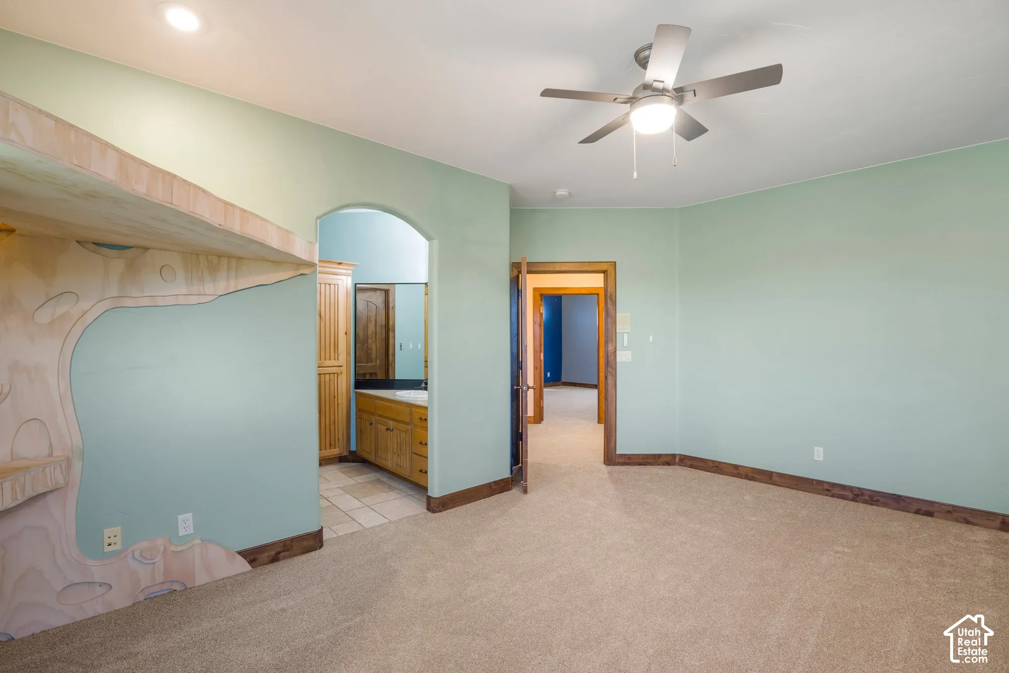 Room featuring arched passage, vaulted ceilings, integrated ceiling fan with light fixture, neutral carpeting, and custom woodwork