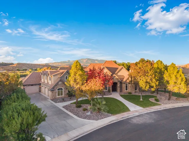 Multi-gabled residence with stone masonry facade, clay tile roof, concrete driveway, attached multi-car garage, and landscaped grounds featuring mountain scenery
