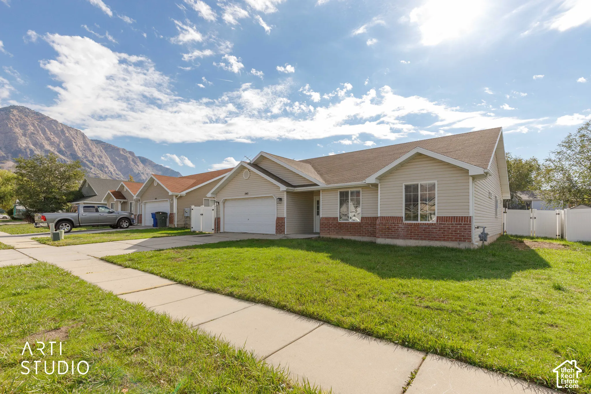 Single-story residence featuring light-toned vinyl siding, brick masonry lower exterior, two-car garage, and mountain backdrop