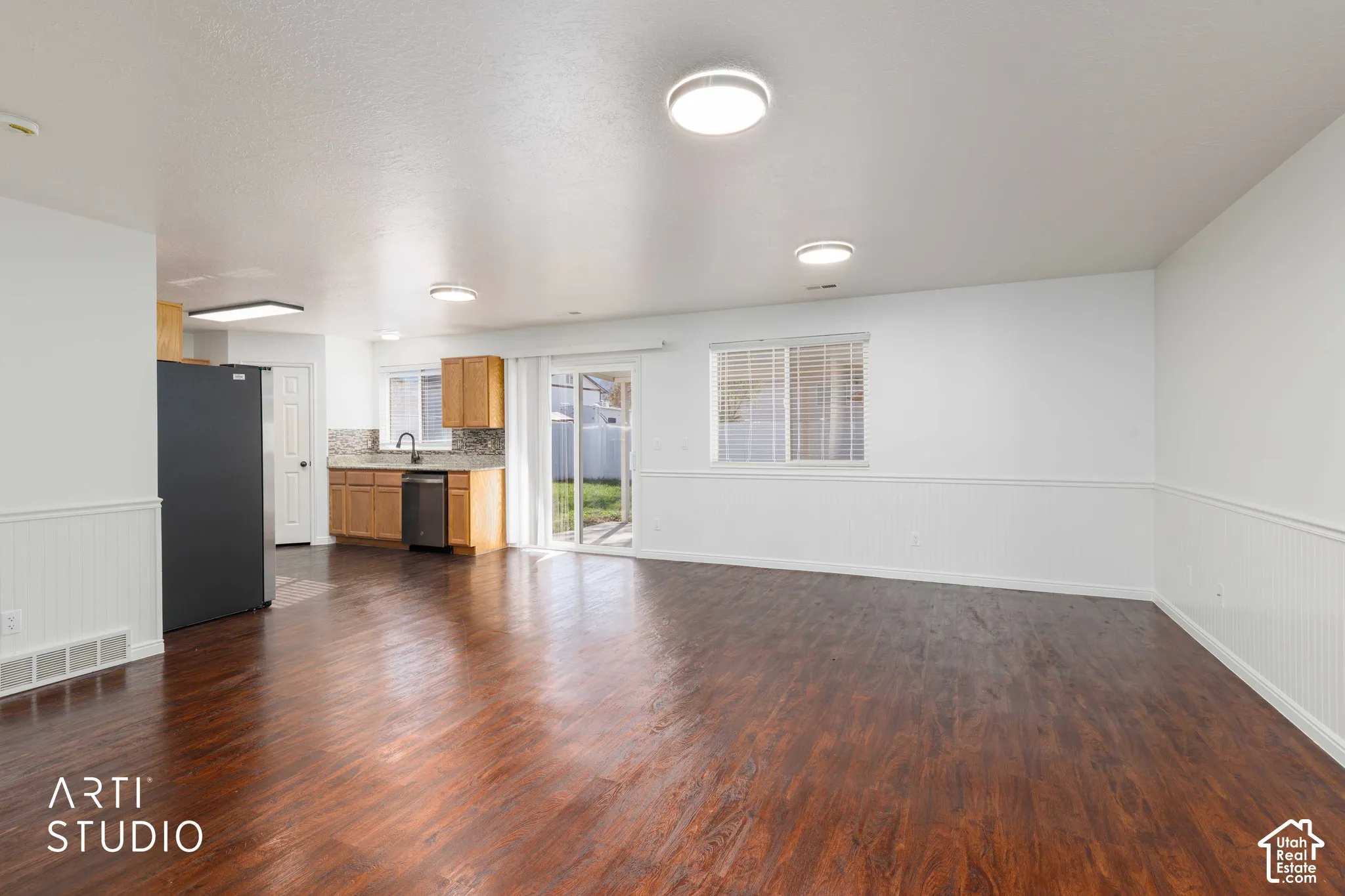 Open-concept interior featuring wood-finish flooring, wainscoting, sliding glass doors, and kitchen cabinetry with integrated appliances