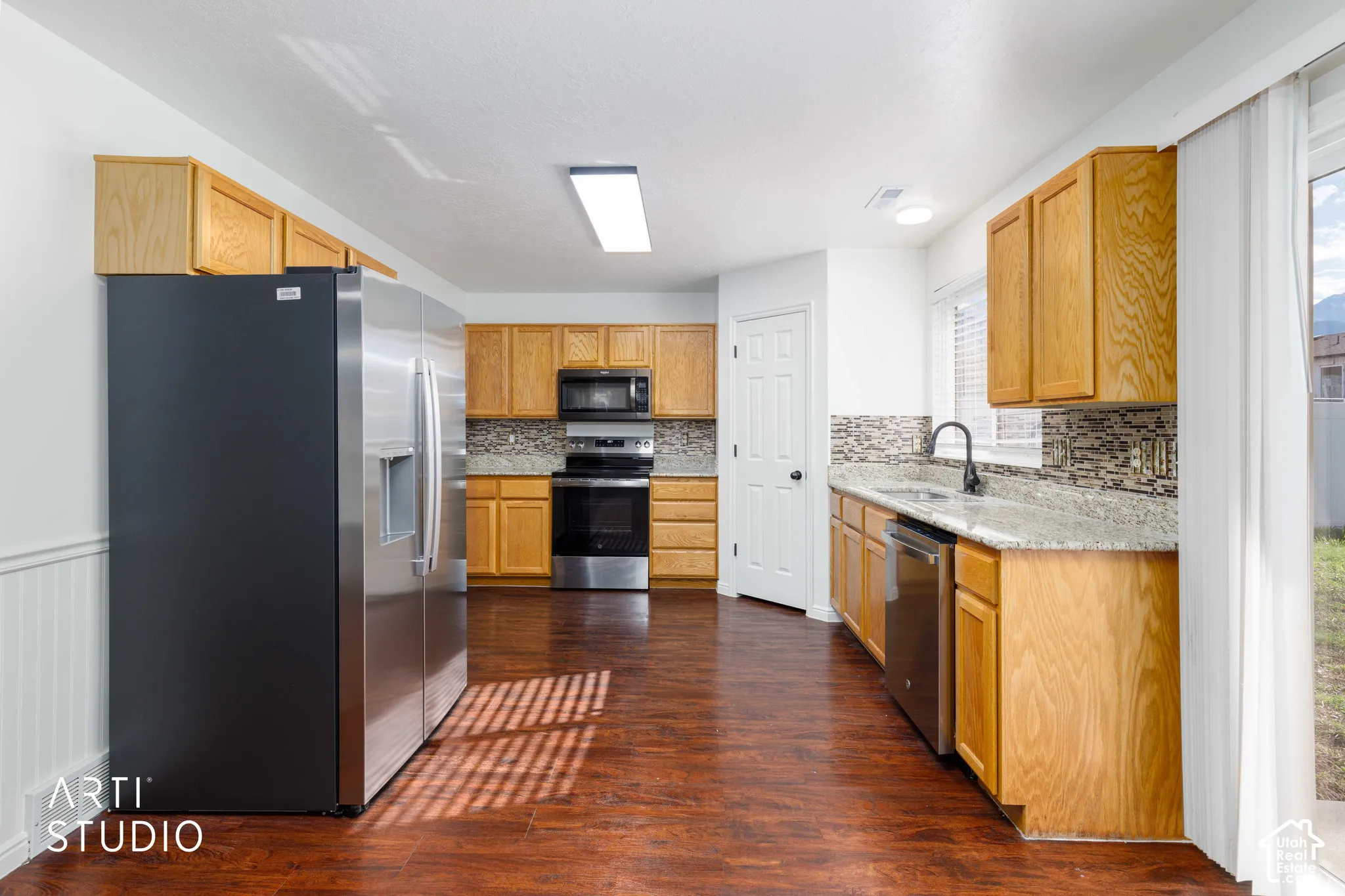 Kitchen featuring wood cabinetry, stone-surface countertops, stainless steel appliances, a mosaic tile backsplash, and wood-finish flooring