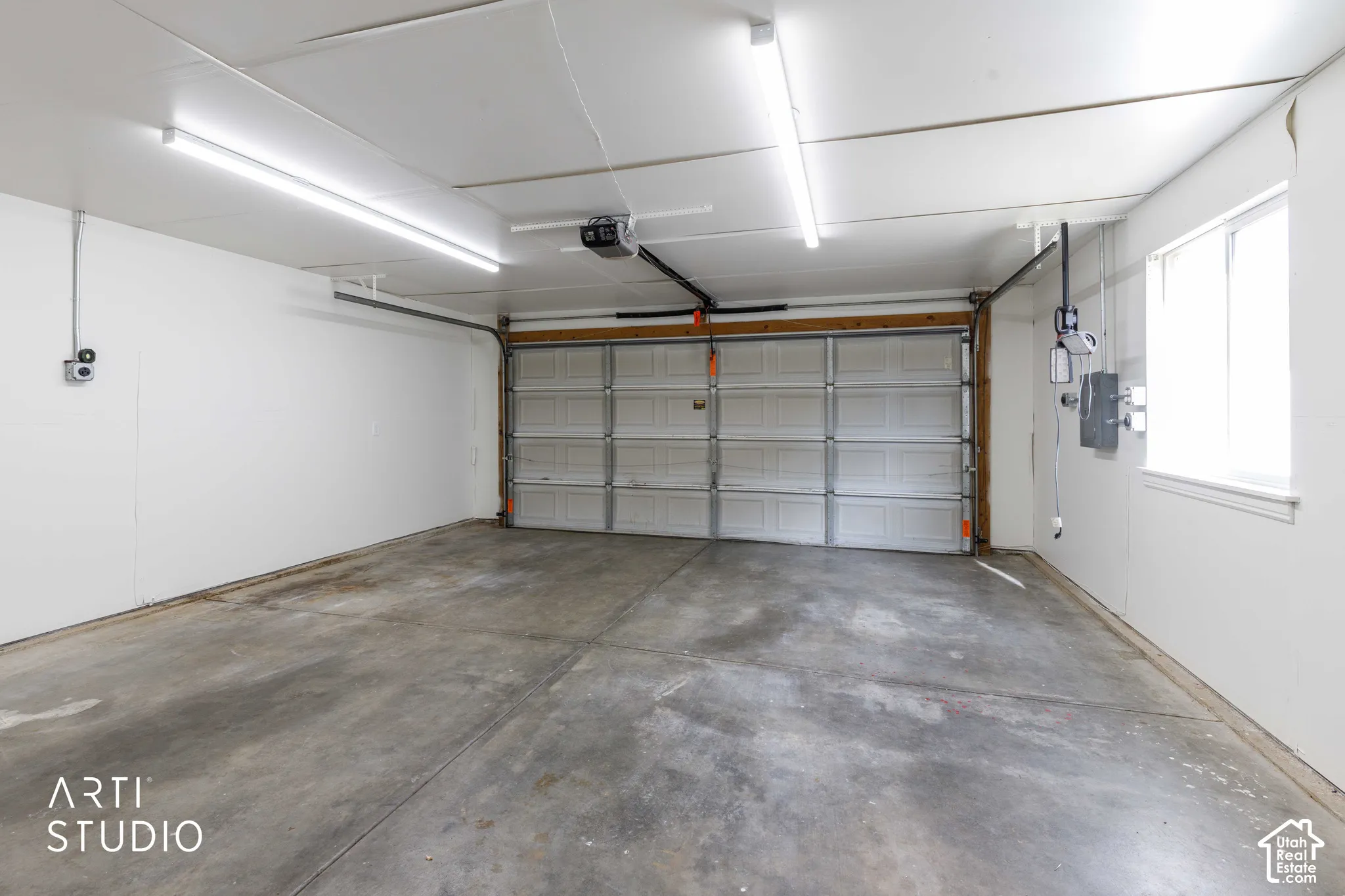 Enclosed garage featuring concrete flooring, white walls, paneled overhead door, and linear overhead lighting