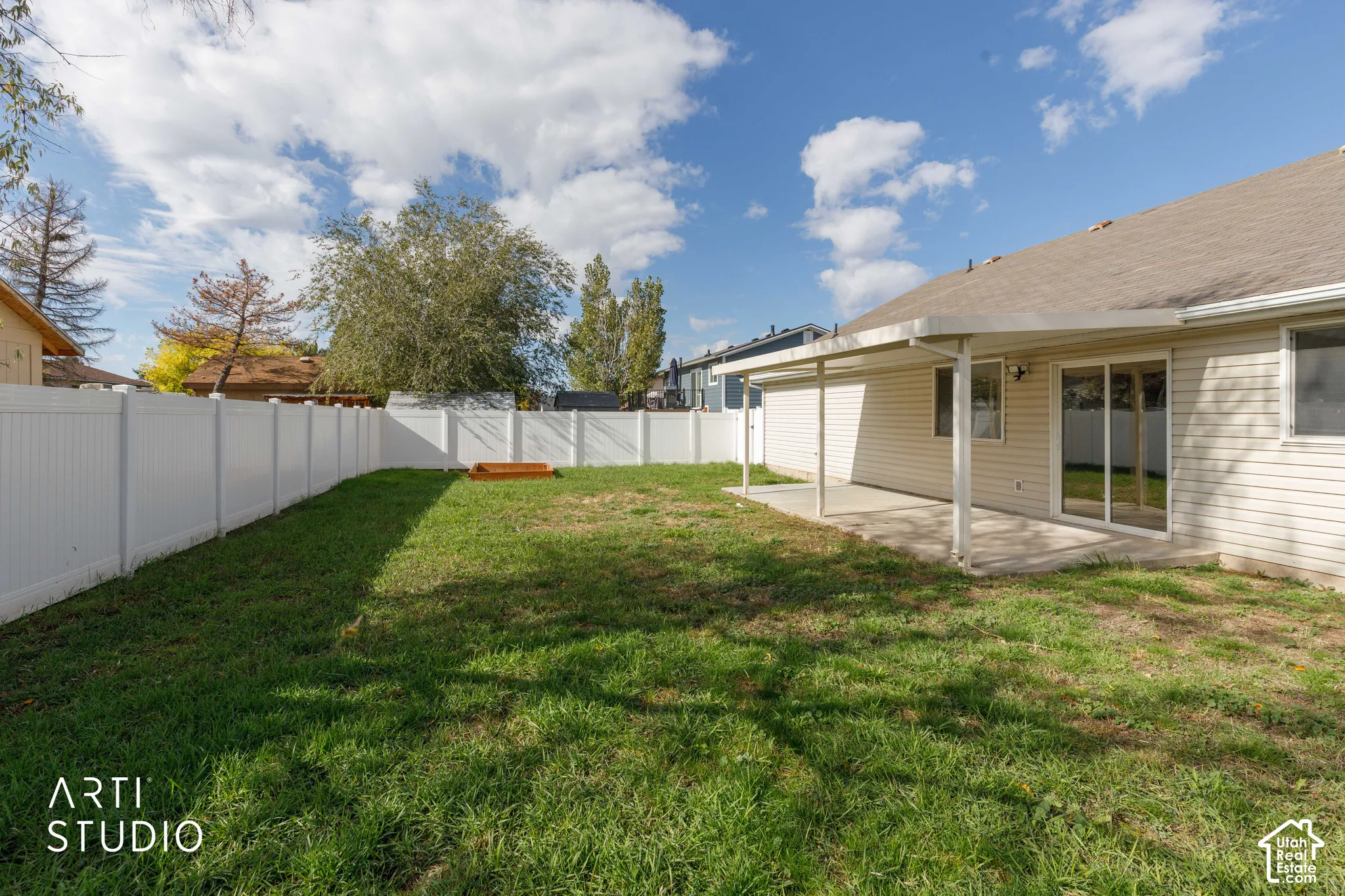 Rear exterior featuring a covered concrete patio, white vinyl privacy fencing, and an open lawn area