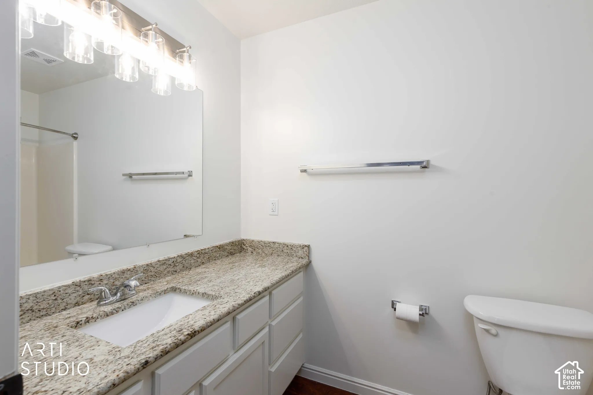 Vanity featuring a stone-surface countertop, integrated rectangular sink, chrome-finish faucet, and shaker-style cabinetry, complemented by a large wall-mounted mirror and multi-bulb fixture