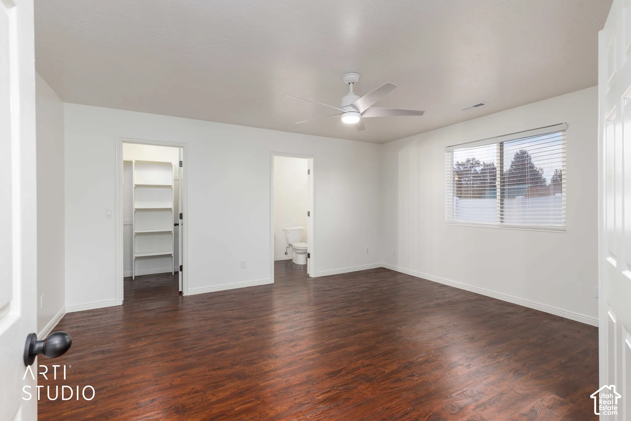 Room featuring wood-finish flooring, a ceiling fan with integrated lighting, a window with horizontal blinds, and built-in closet shelving