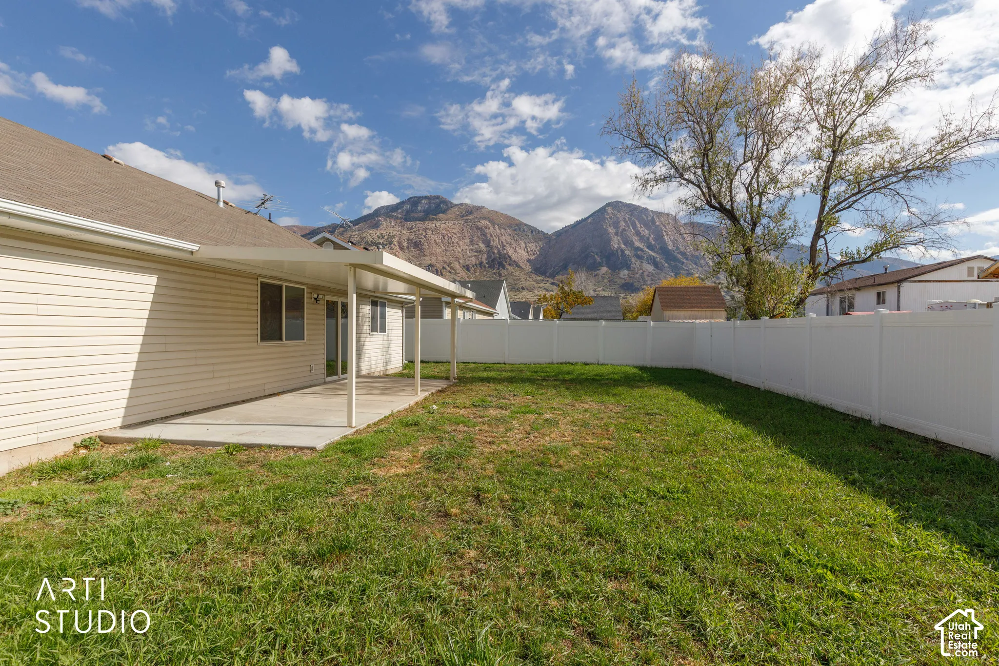 Rear yard featuring a concrete patio, covered metal awning, vinyl privacy fencing, and mountain backdrop