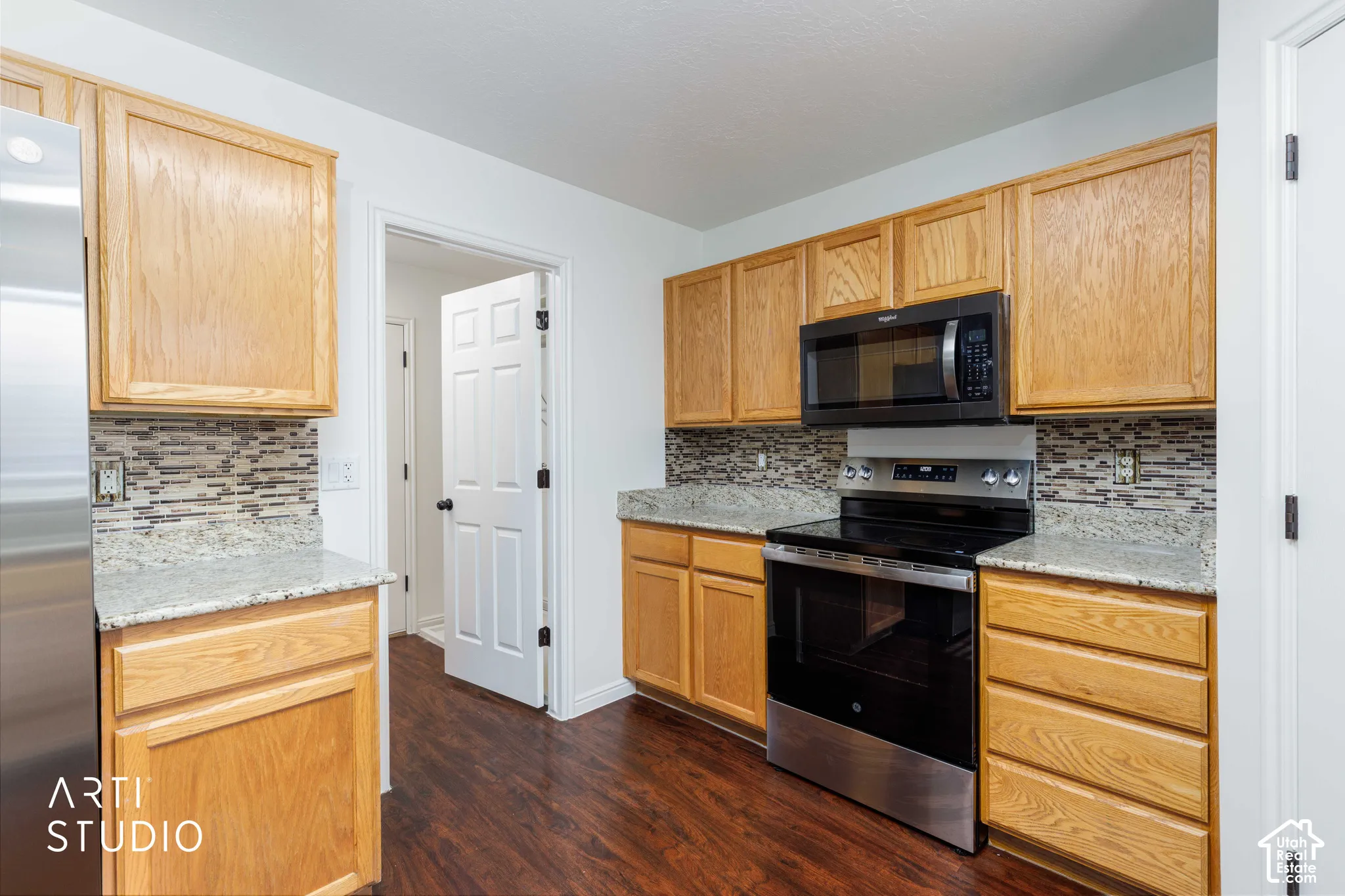 Kitchen featuring light-tone wood cabinetry, stone countertops, a mosaic tile backsplash, and stainless steel appliances