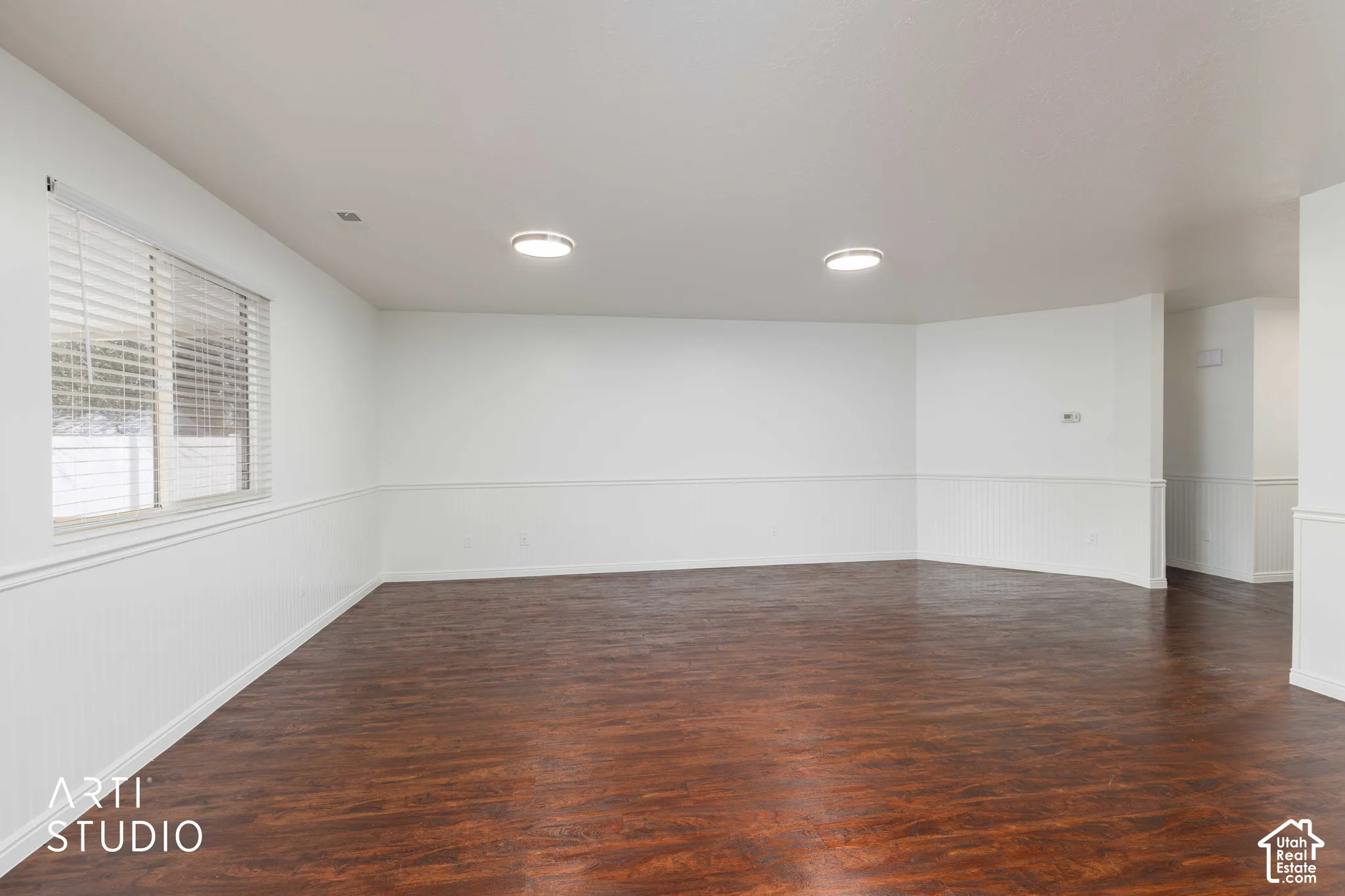 Interior room featuring wood-finish flooring, white beadboard wainscoting, flush-mount ceiling lighting, and horizontal window blinds