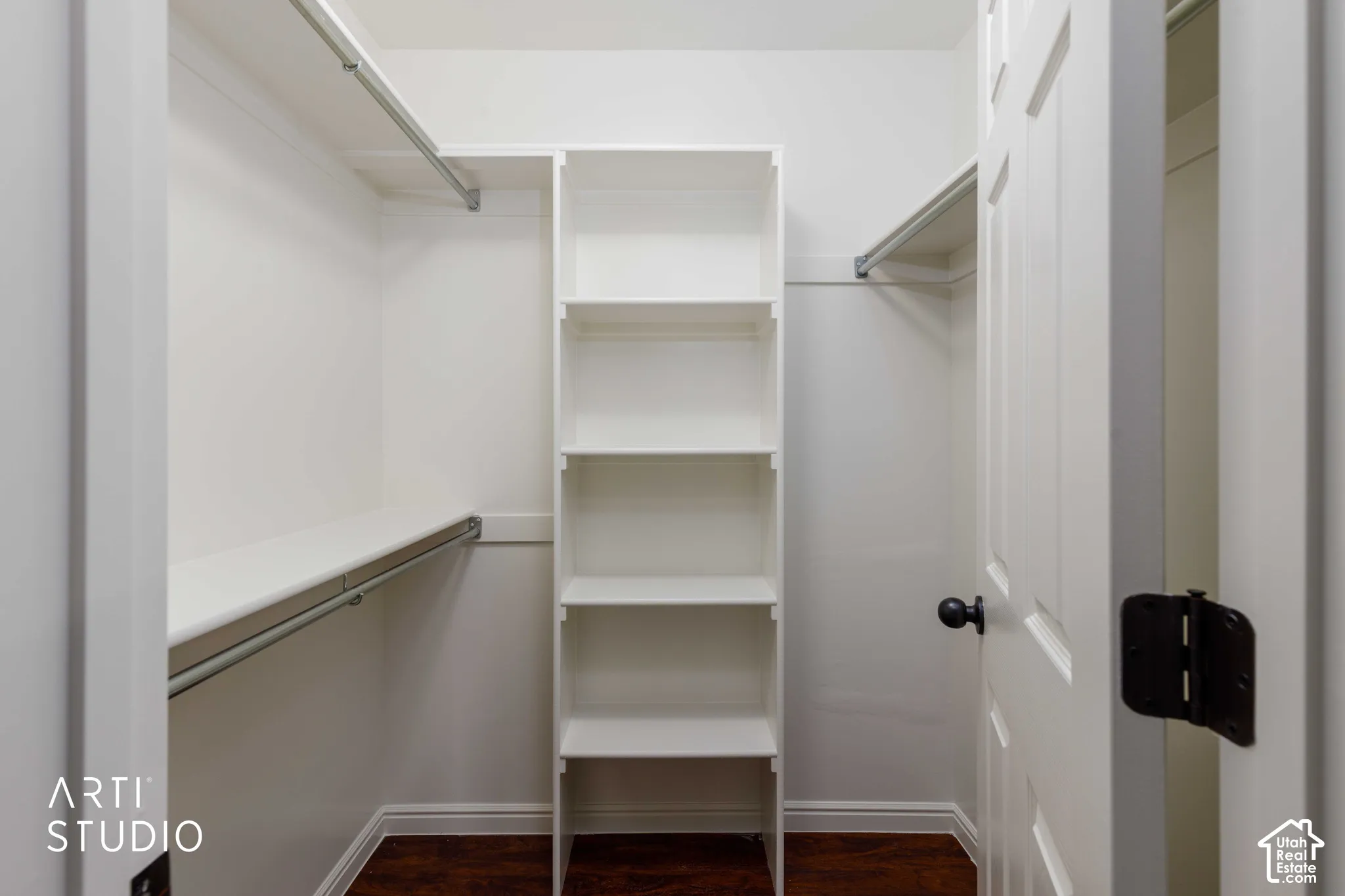 Walk-in closet featuring white built-in shelving, dual-level metal hanging rods, and wood-finish flooring