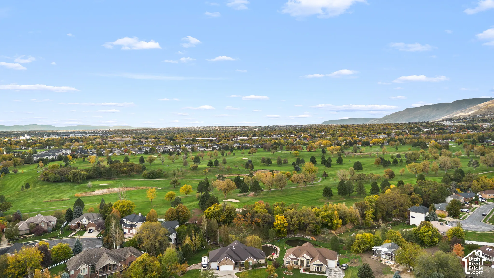 Aerial perspective featuring expansive golf course fairways, mature tree canopy, and mountainous horizon
