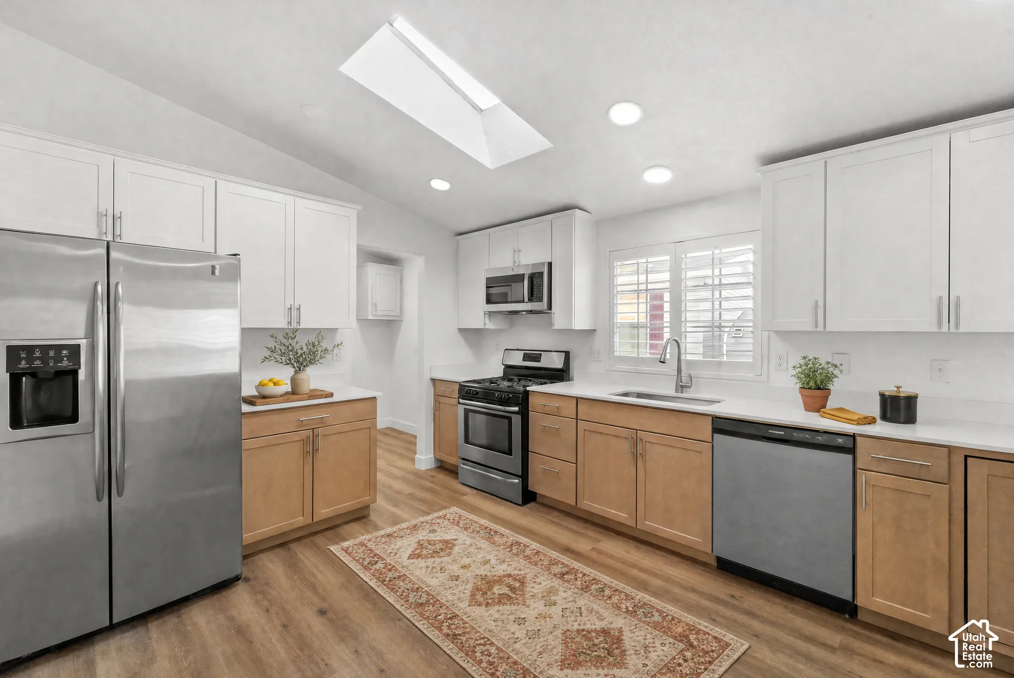 Kitchen featuring two-tone cabinetry, stainless steel appliances, quartz countertops, wood-finish flooring, and a skylight