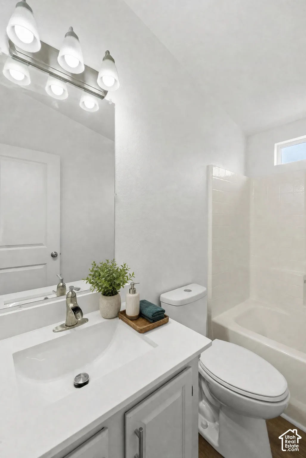 Bathroom featuring a white vanity with a rectangular sink, brushed nickel faucet, large wall-mounted mirror, multi-bulb light fixture, and a white tile tub-shower combination