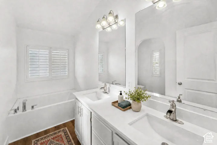 Bathroom featuring a dual-sink vanity with white cabinetry, a composite countertop, polished metal fixtures, and plantation shutters