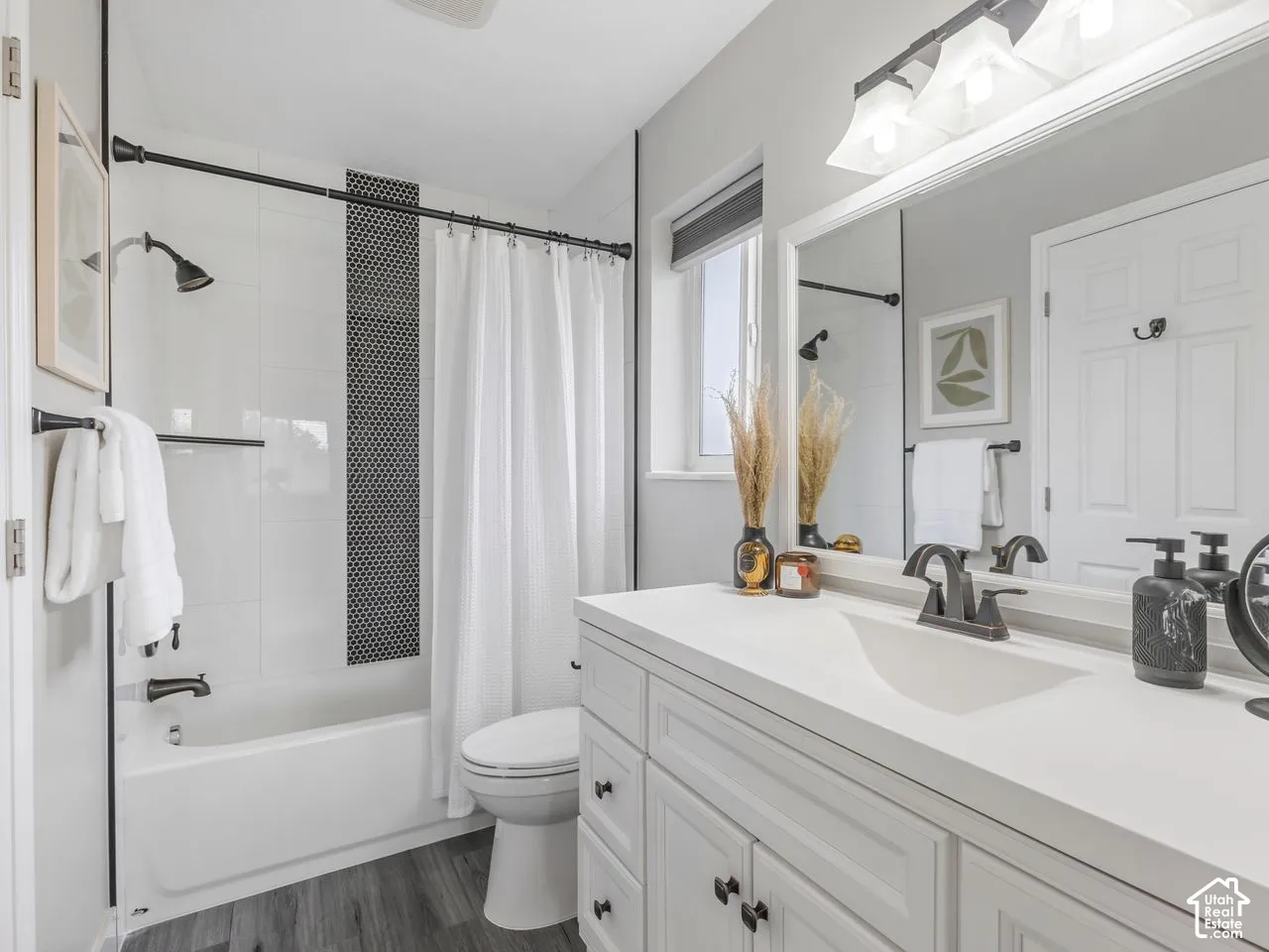 Bathroom featuring a white vanity with an integrated basin, matte black fixtures, wood-finish flooring, and a tub-shower combination with a vertical tile accent
