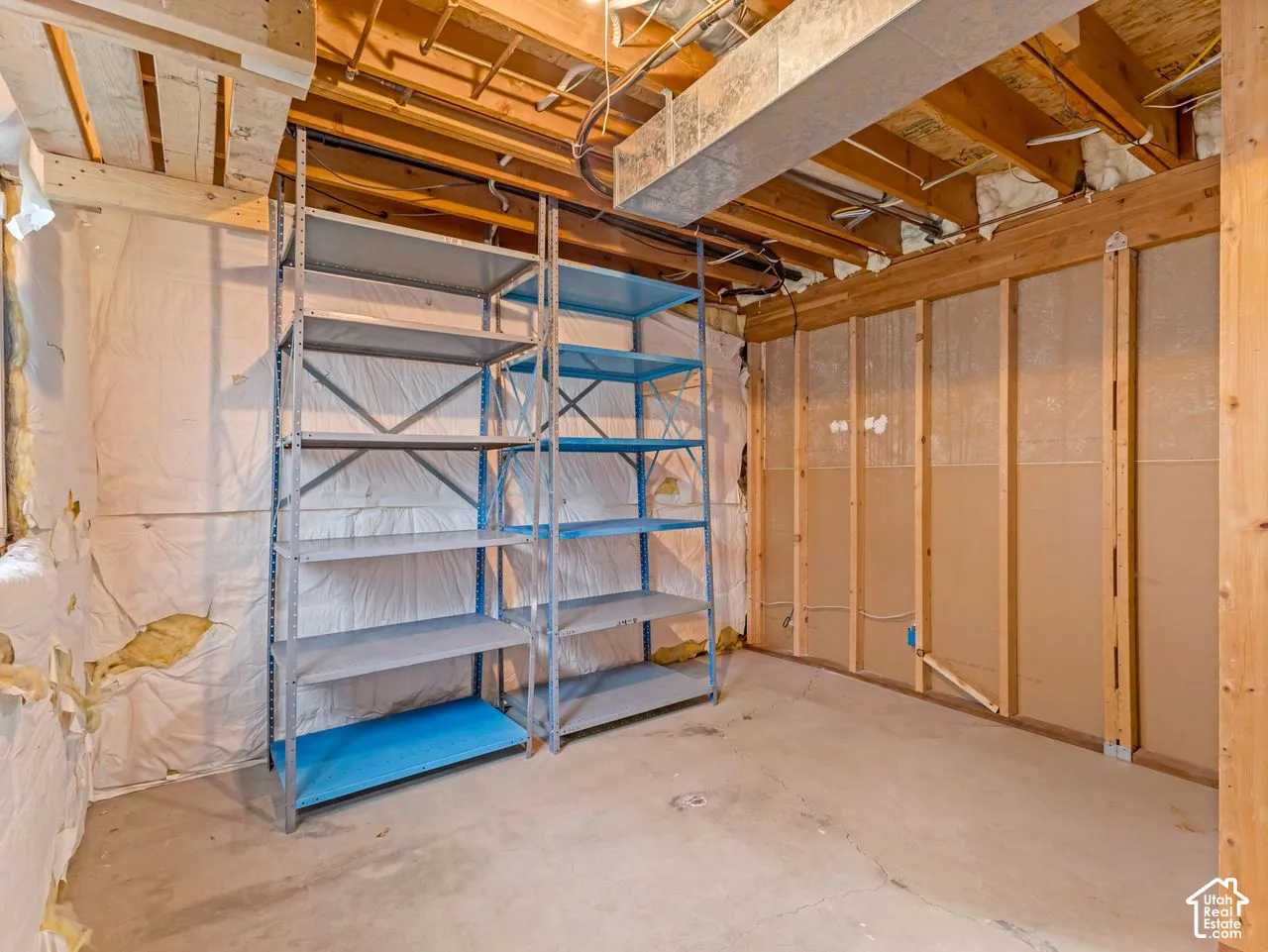 Storage area featuring concrete flooring, unfinished wood framing, exposed joists, and metal industrial shelving units
