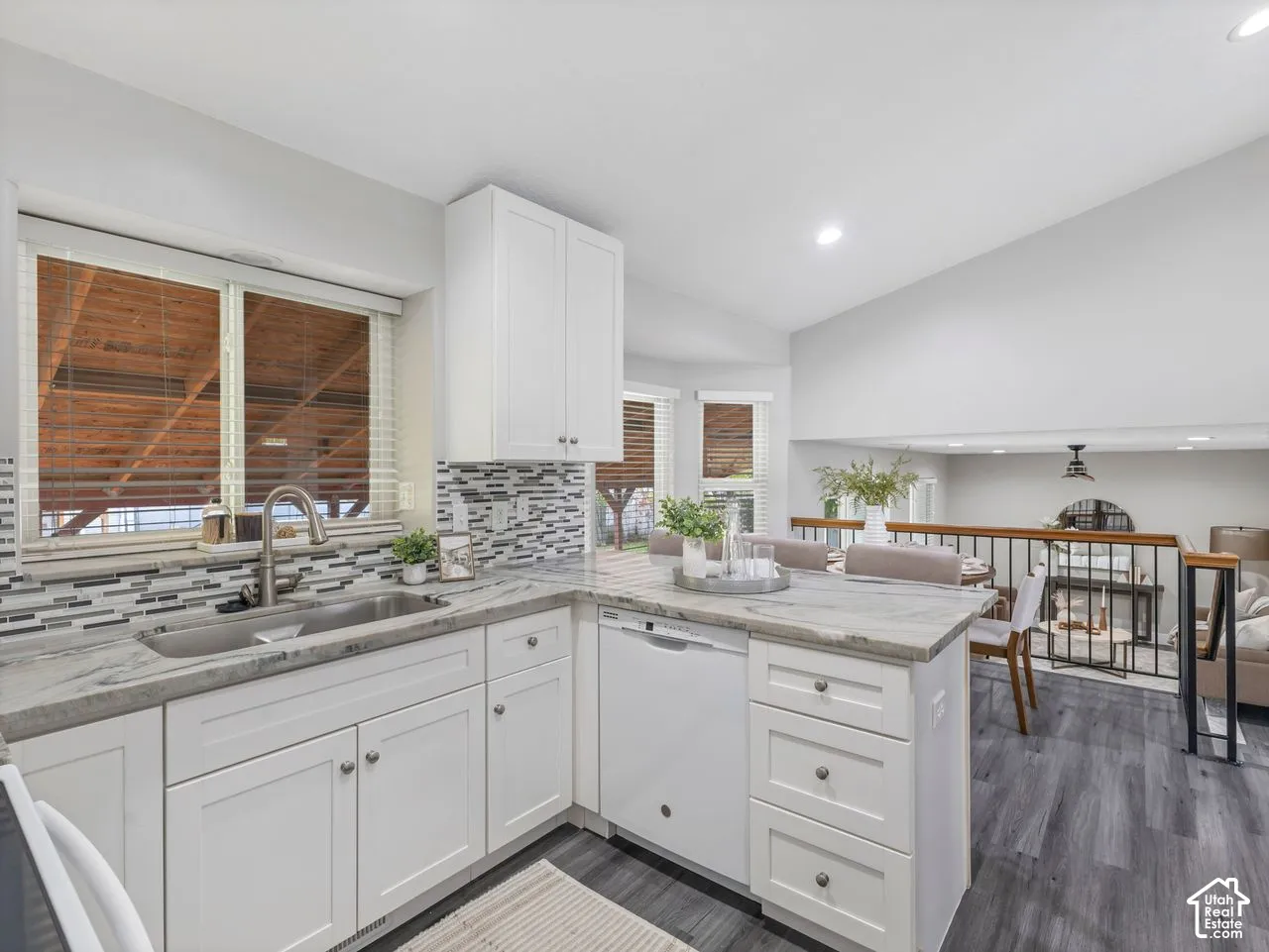 Kitchen featuring white shaker cabinetry, stone-patterned countertops, a multi-tone linear tile backsplash, stainless steel undermount sink, and wood-finish flooring