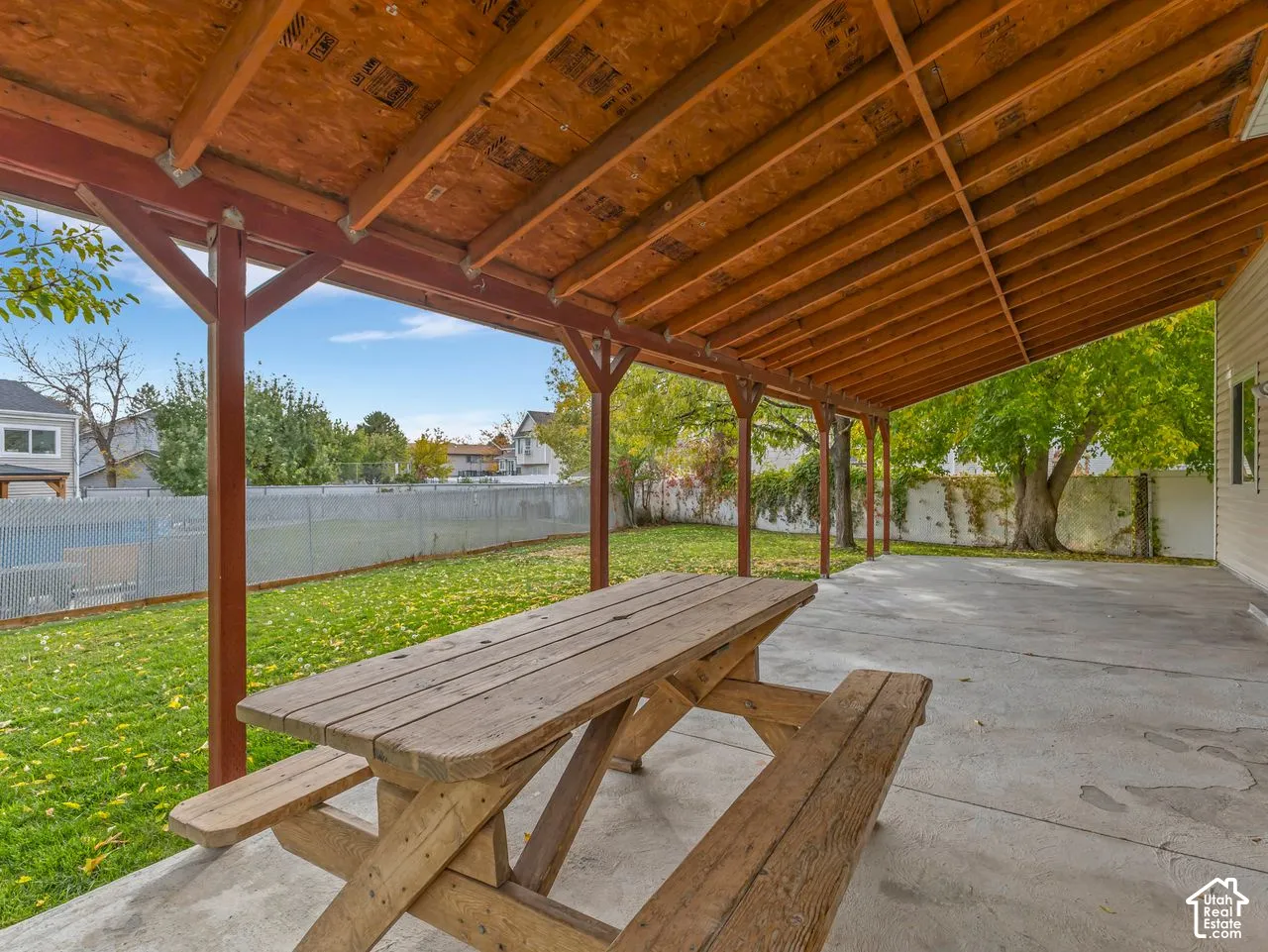 Covered concrete patio featuring exposed wood-beam ceiling construction and a fenced backyard