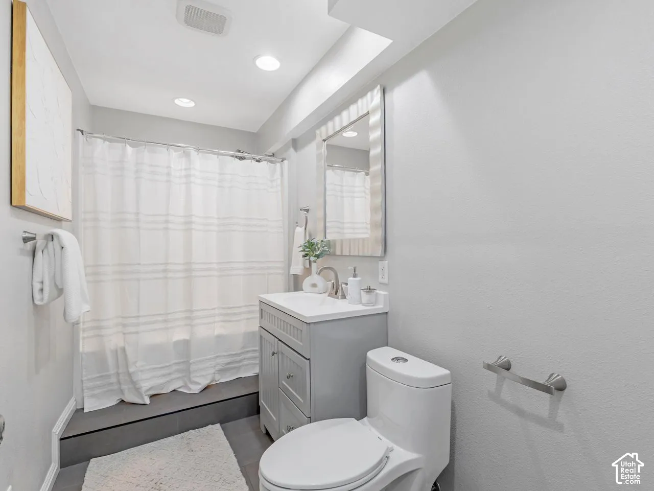 Vanity with an integrated sink, rectangular wall-mounted mirror, recessed ceiling lighting, and a bathtub with a tiled surround