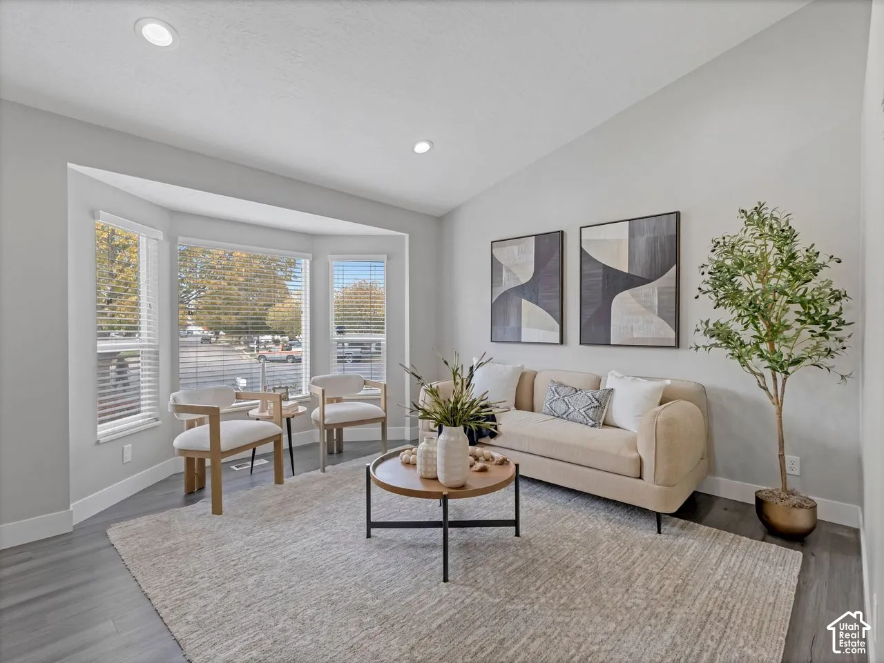 Vaulted ceiling with recessed lighting, bay window, and wood-finish flooring