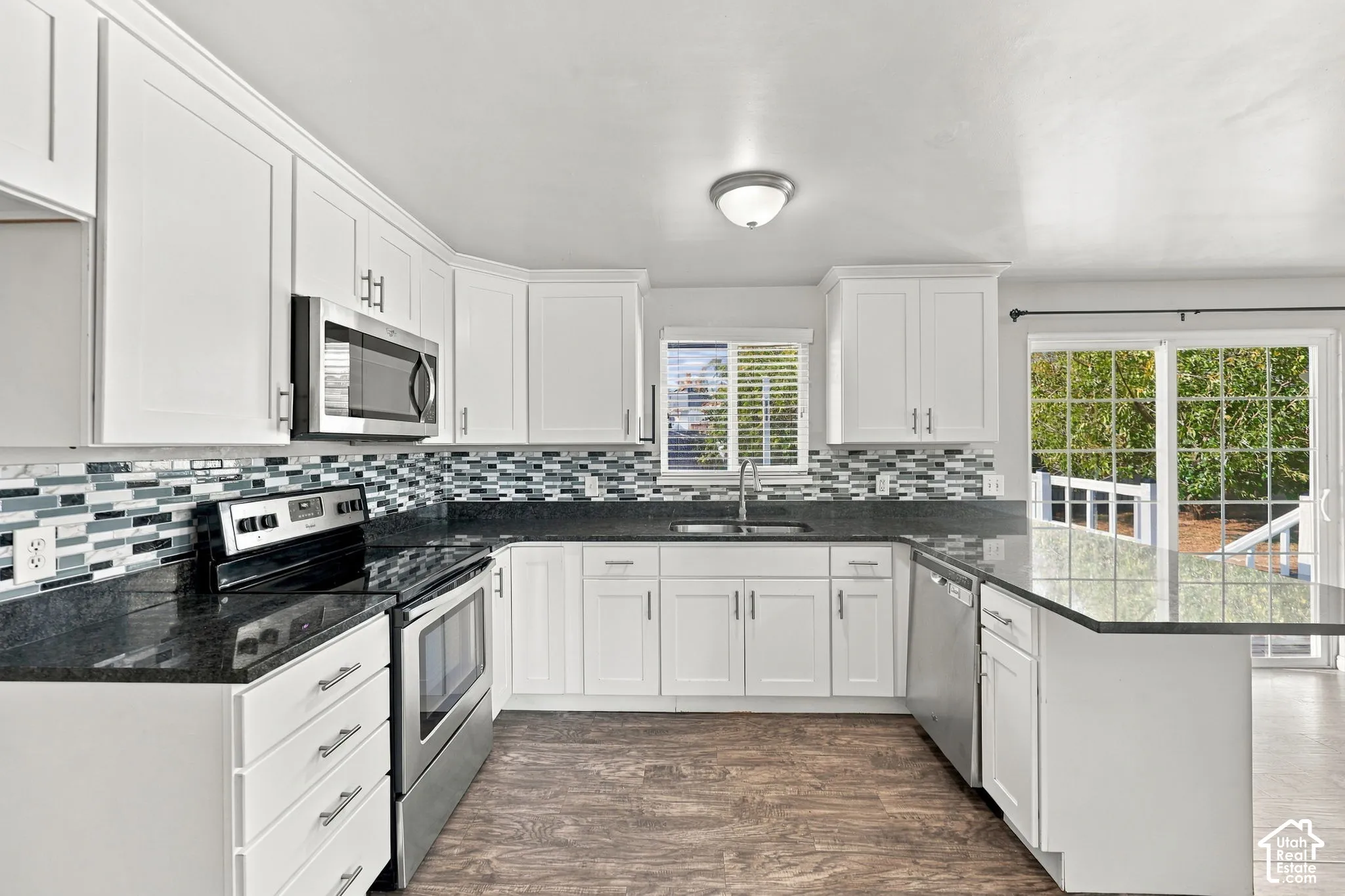 Kitchen with stainless steel range, microwave, and dishwasher, mosaic tile backsplash, and window over the sink