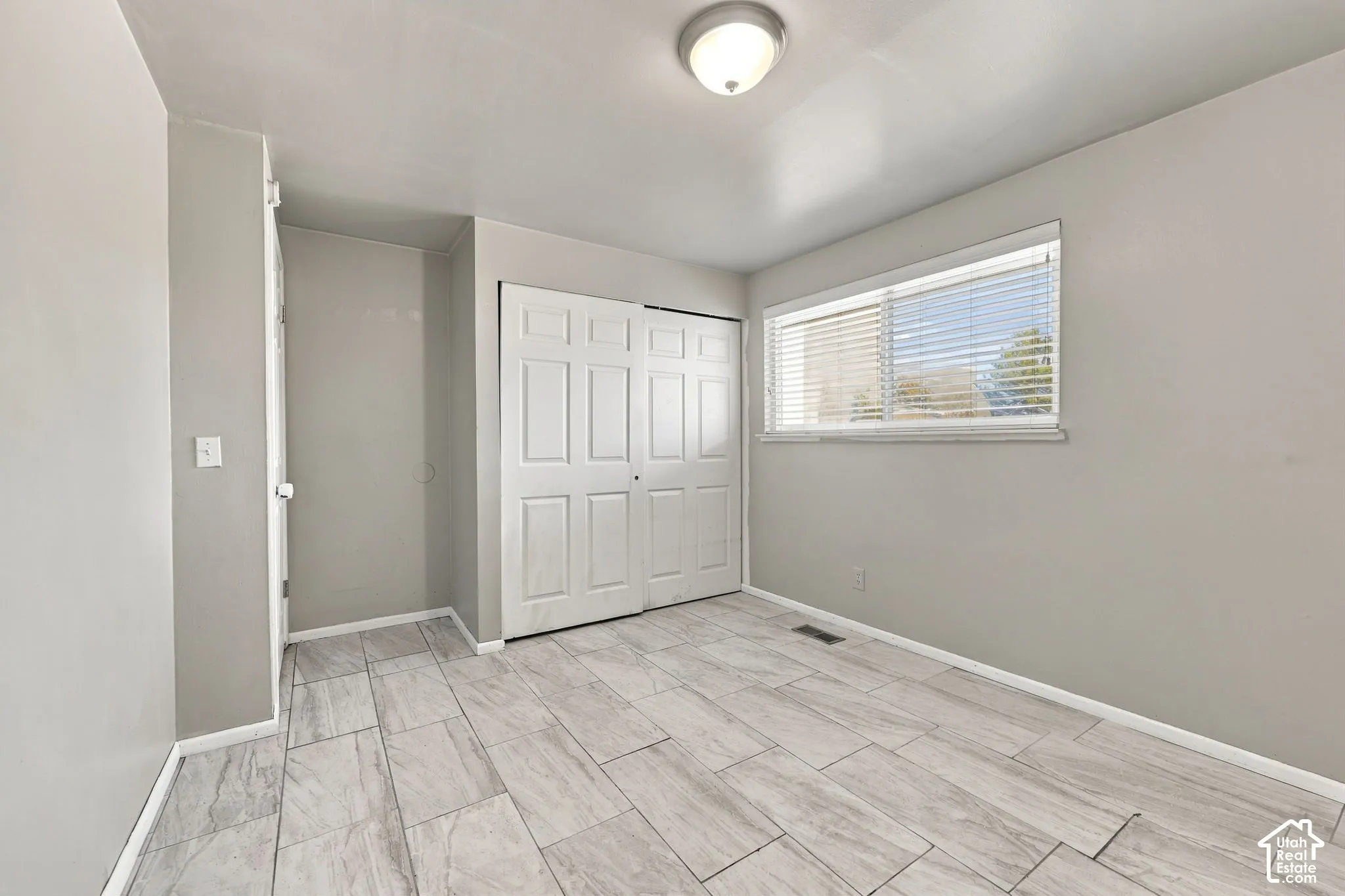 Bedroom with wood-look tile flooring, double closet doors, and window with blinds