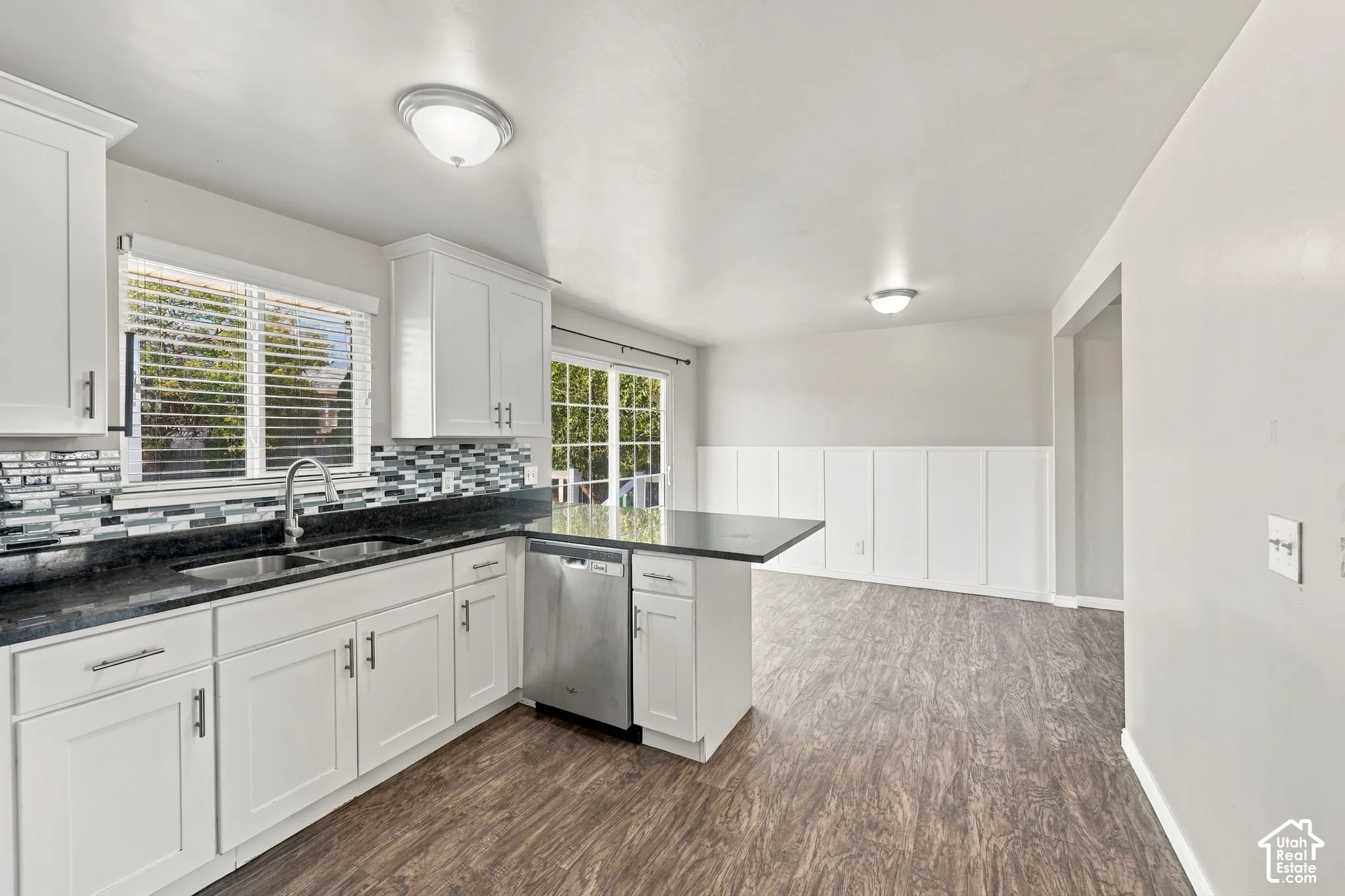Kitchen sink area with window, stainless steel dishwasher, dark countertops, and white cabinetry