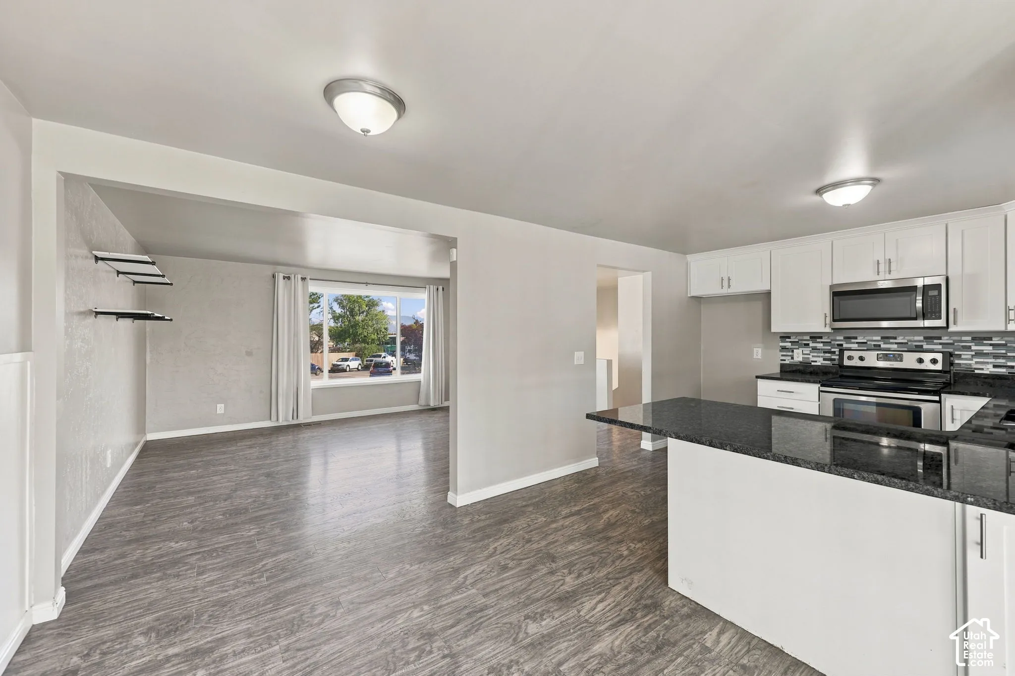 Kitchen open to the living room, with peninsula, dark countertops, white cabinetry, and stainless steel appliances