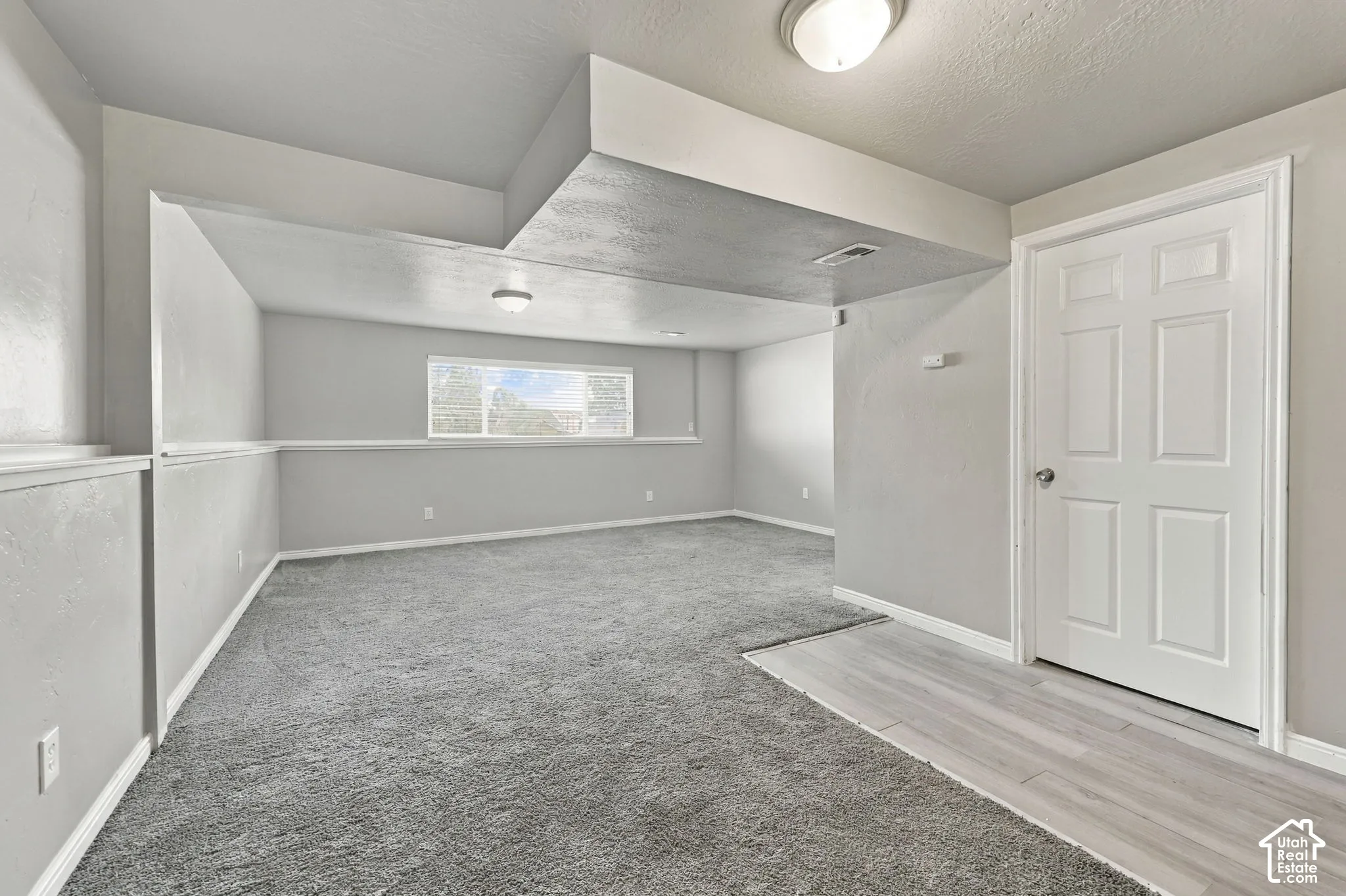 Carpeted room with window alcove, wood-look flooring at the entry, and interior door
