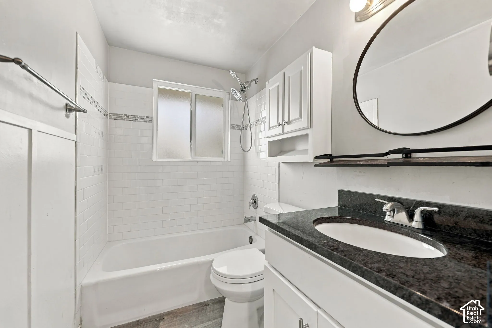 Full bathroom with tub and shower combination, subway tile surround, dark countertop vanity, and over-toilet cabinet