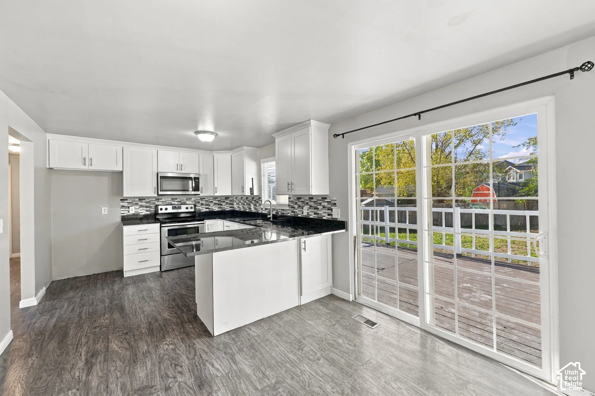 Kitchen with white cabinetry, dark countertops, tile backsplash, and sliding glass door to the rear deck