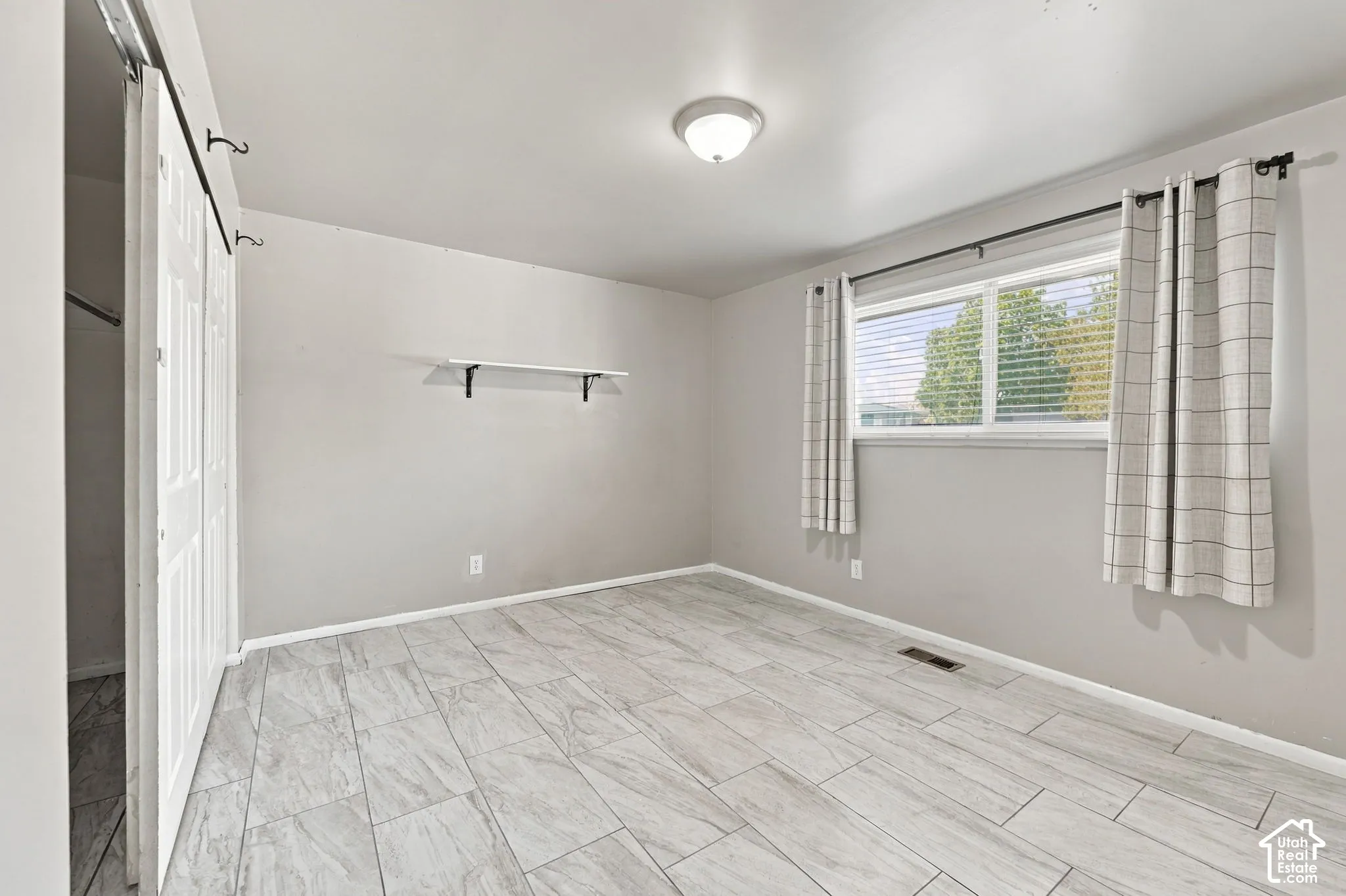 Bedroom with wood-look tile flooring, closet doors, wall shelf, and window