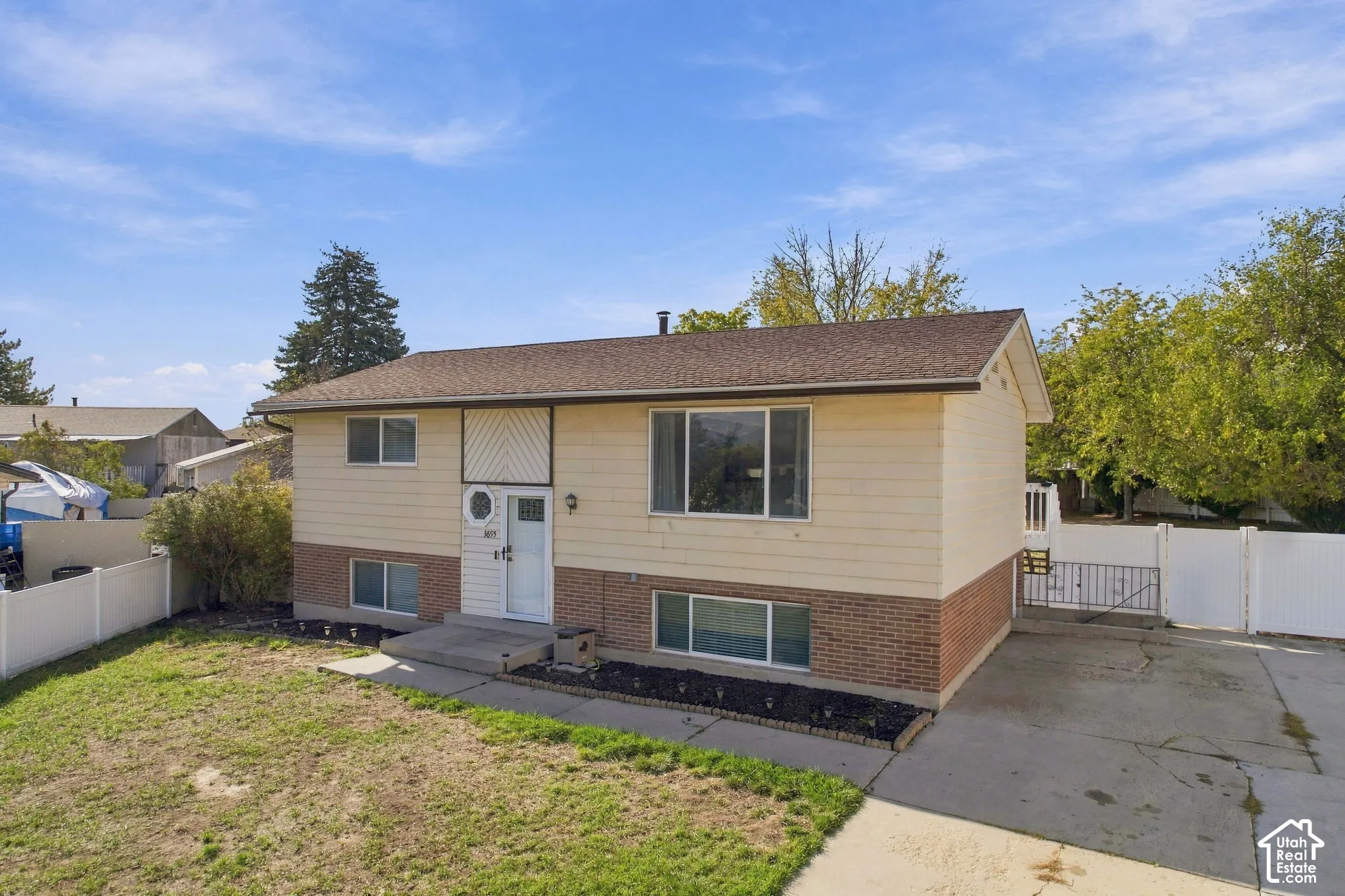 Front exterior with brick and siding, asphalt shingle roof, concrete driveway, and white vinyl fencing