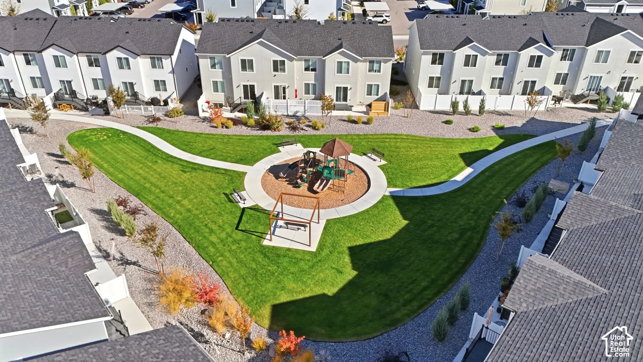 Common area featuring a manicured lawn, concrete walking paths, a playground structure, and metal benches