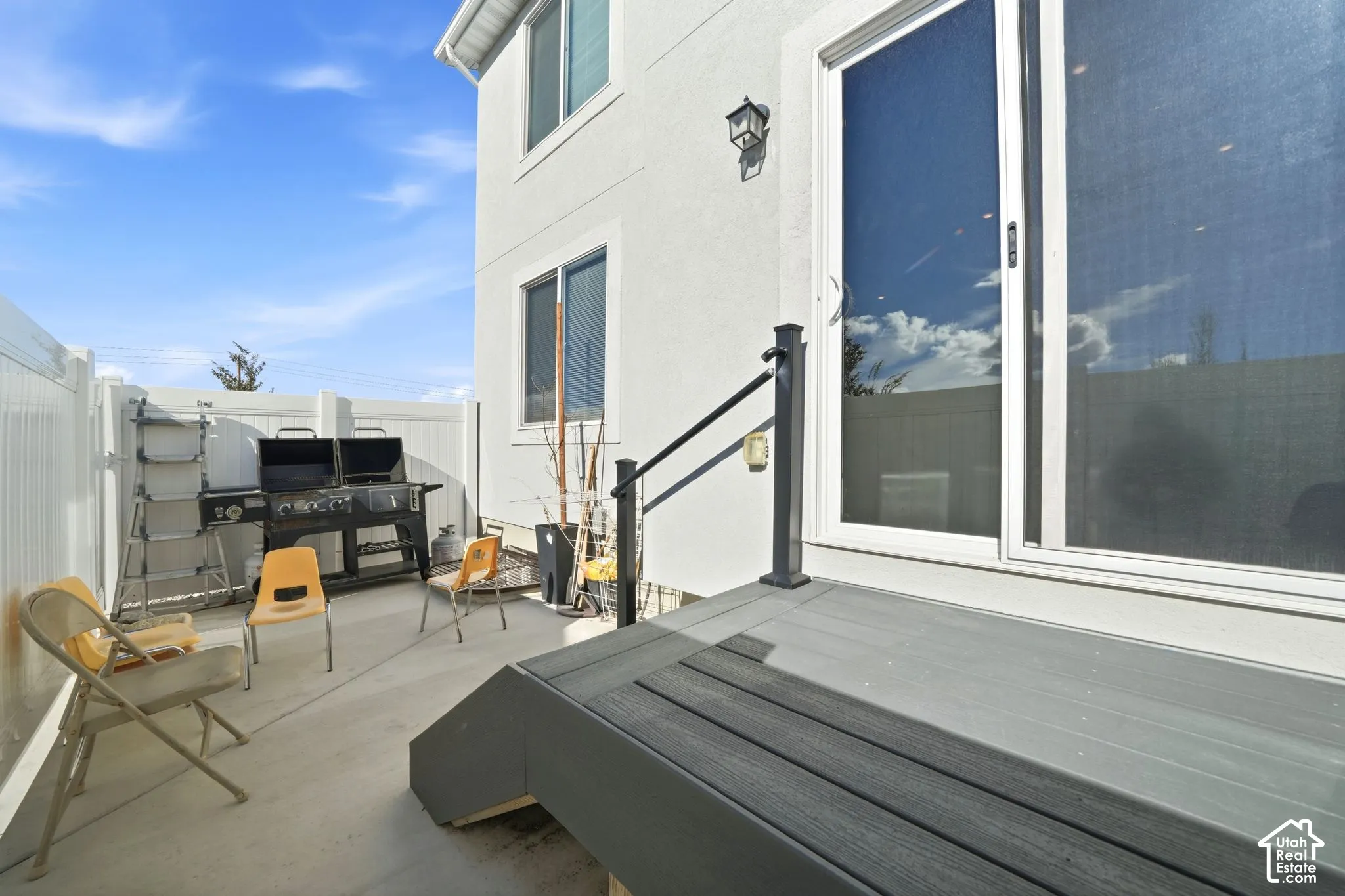 Concrete patio featuring a privacy fence, exterior light fixture, and a composite deck step with a metal handrail