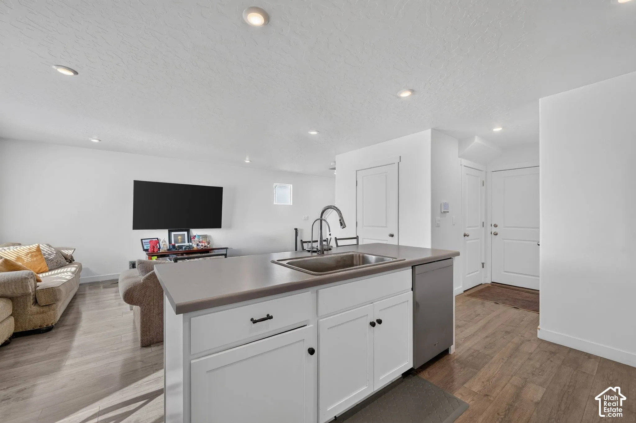 Kitchen island featuring a solid-surface countertop, under-mount stainless steel sink, gooseneck faucet, shaker-style cabinetry, and recessed lighting