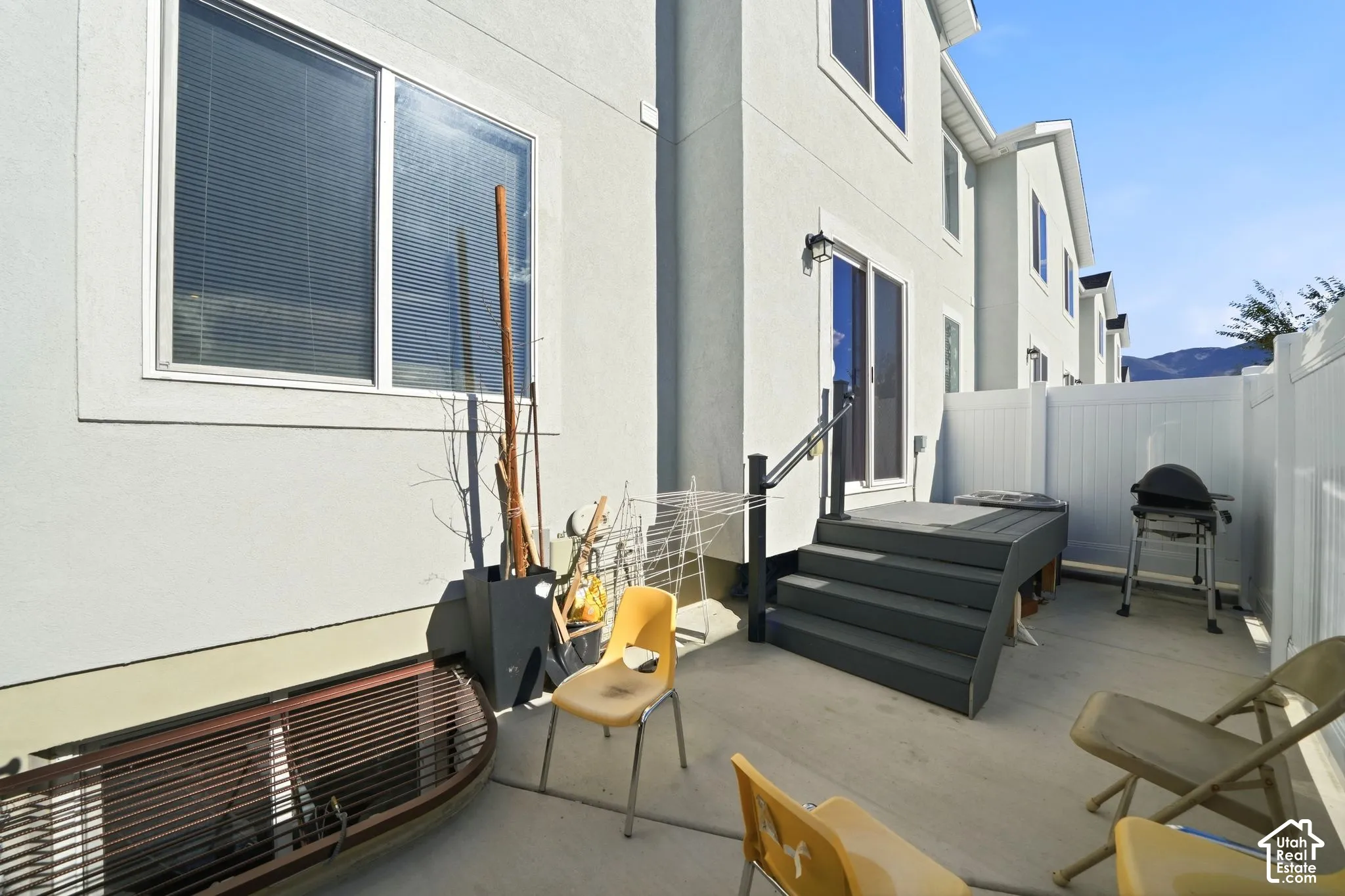 Exterior features include a stucco facade, concrete patio, elevated deck with black metal handrail, and white vinyl privacy fencing