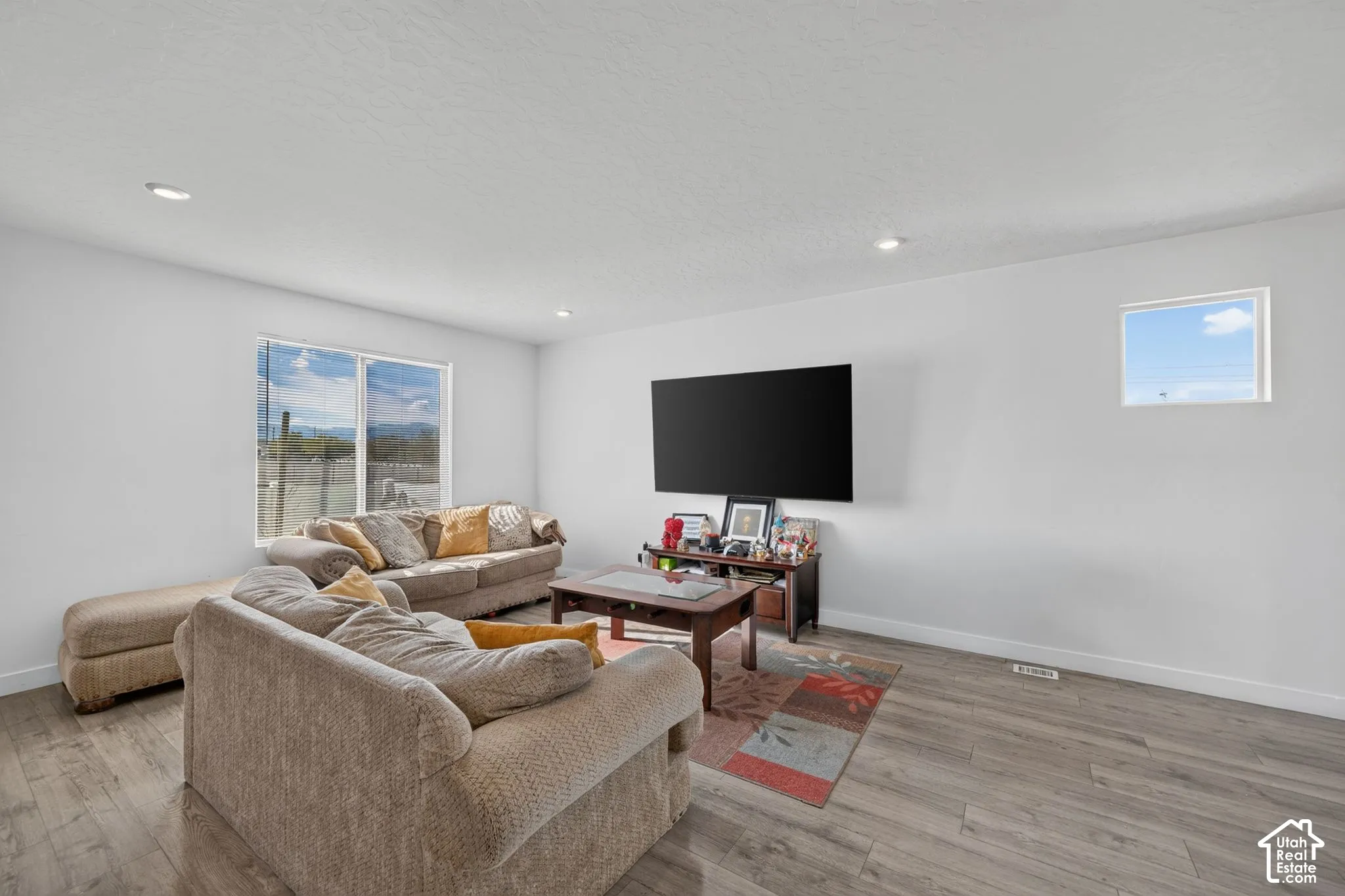 Neutral-toned interior space featuring wood-finish flooring, recessed lighting, and multiple windows