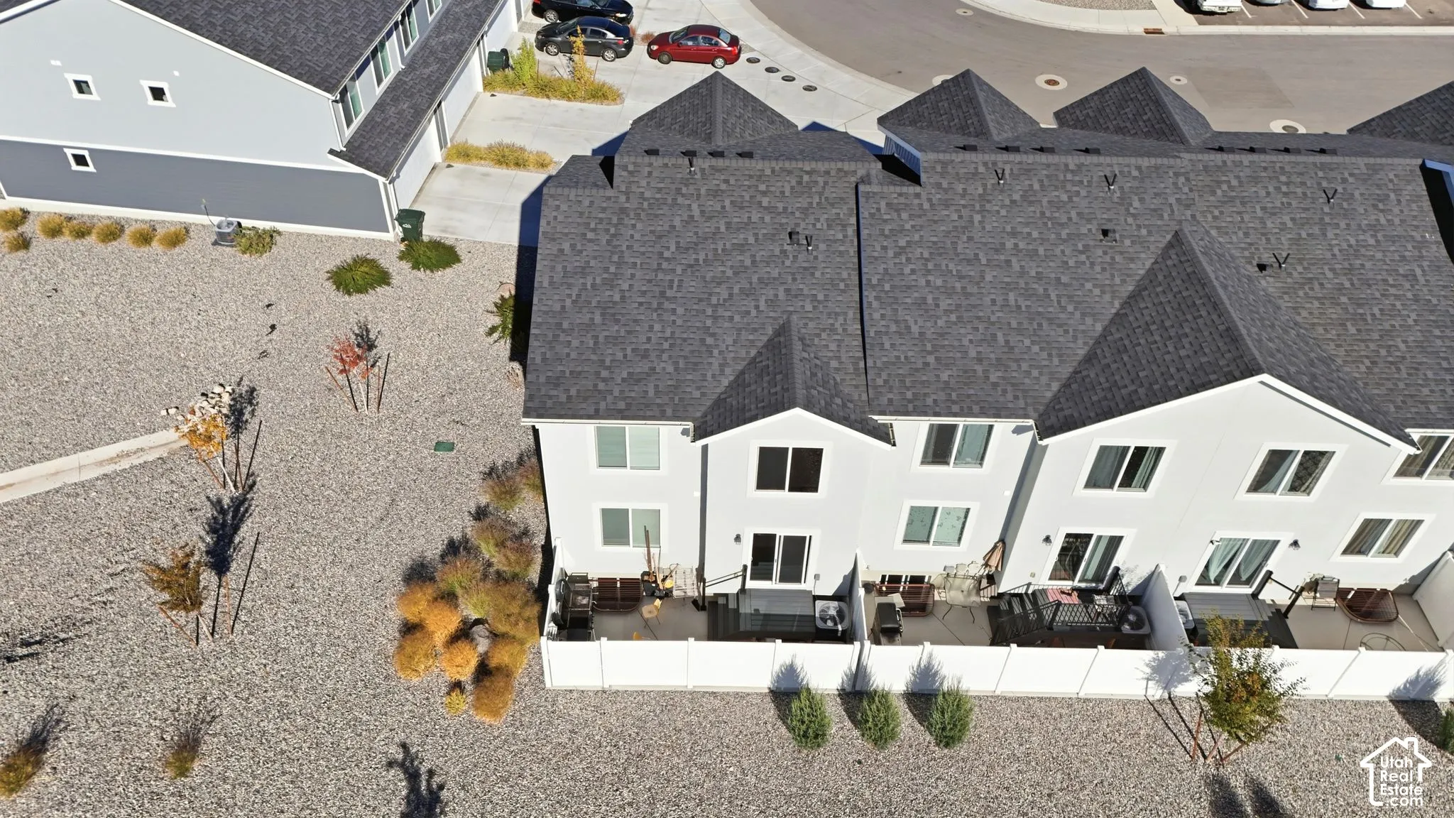 Multi-unit residential exterior featuring a grey shingle roof, white siding, and fenced private patio areas