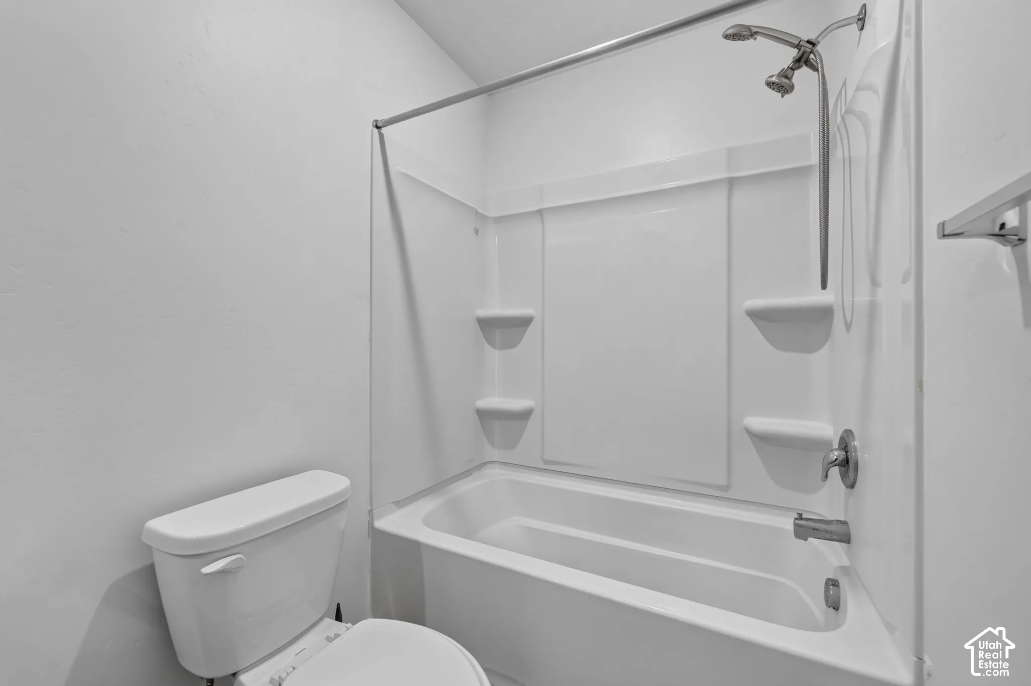 Full bathroom featuring a white porcelain toilet, a composite tub and shower surround with integrated shelving, and a chrome wall-mounted shower fixture