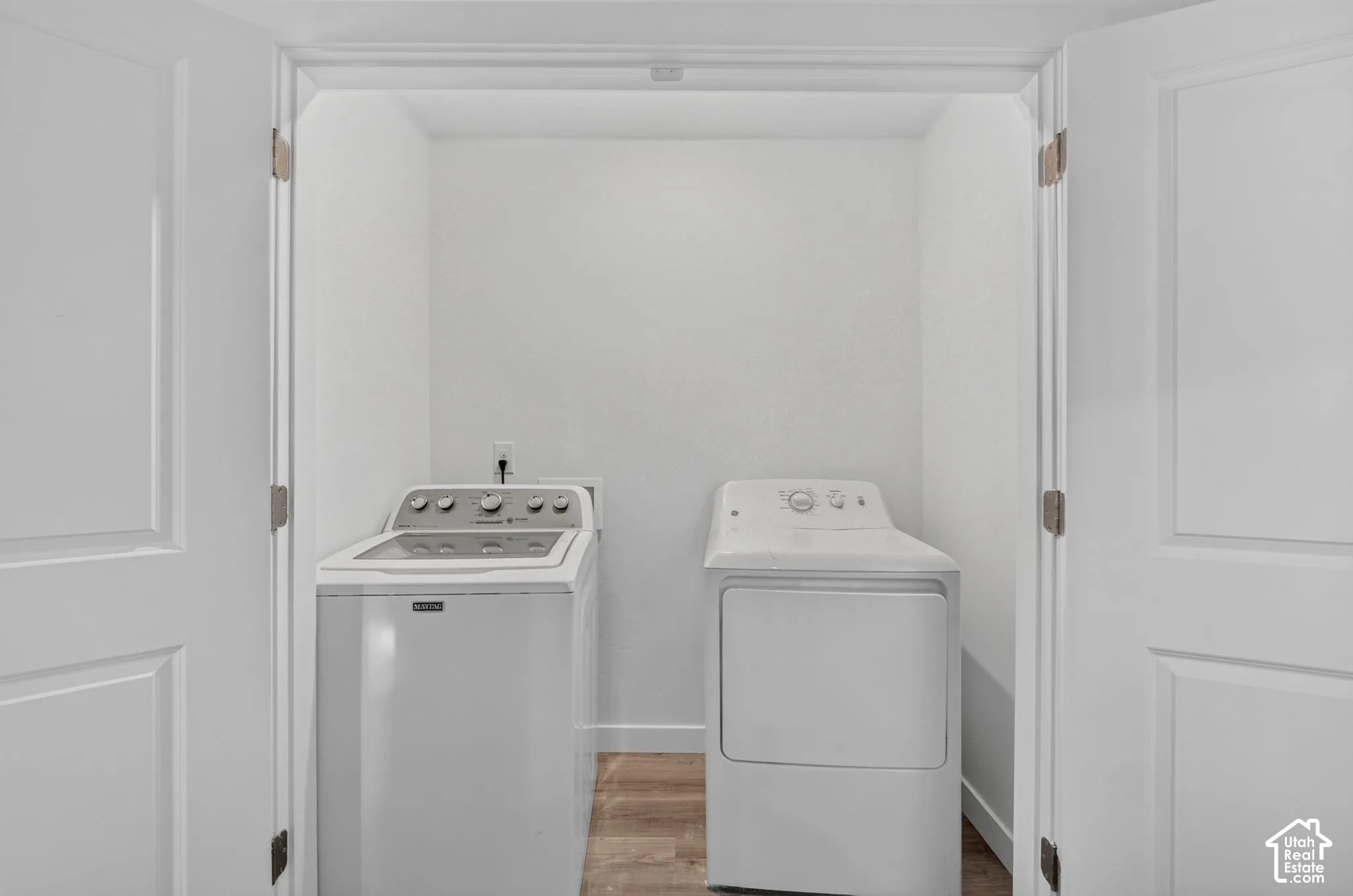 Laundry alcove featuring white double-door entry and wood-finish flooring