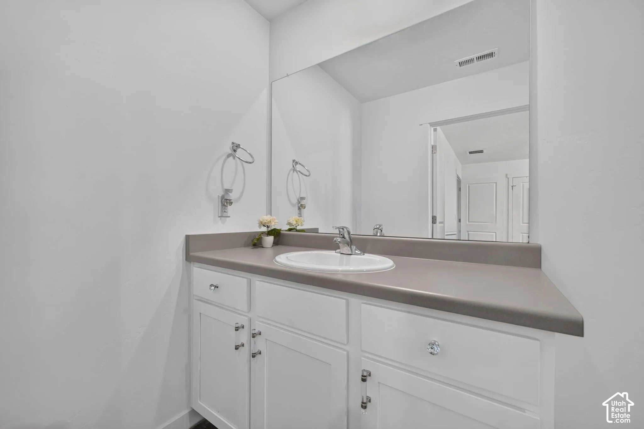 Bathroom vanity featuring white cabinetry, a solid-surface countertop, an integrated drop-in sink, and a large wall-mounted mirror