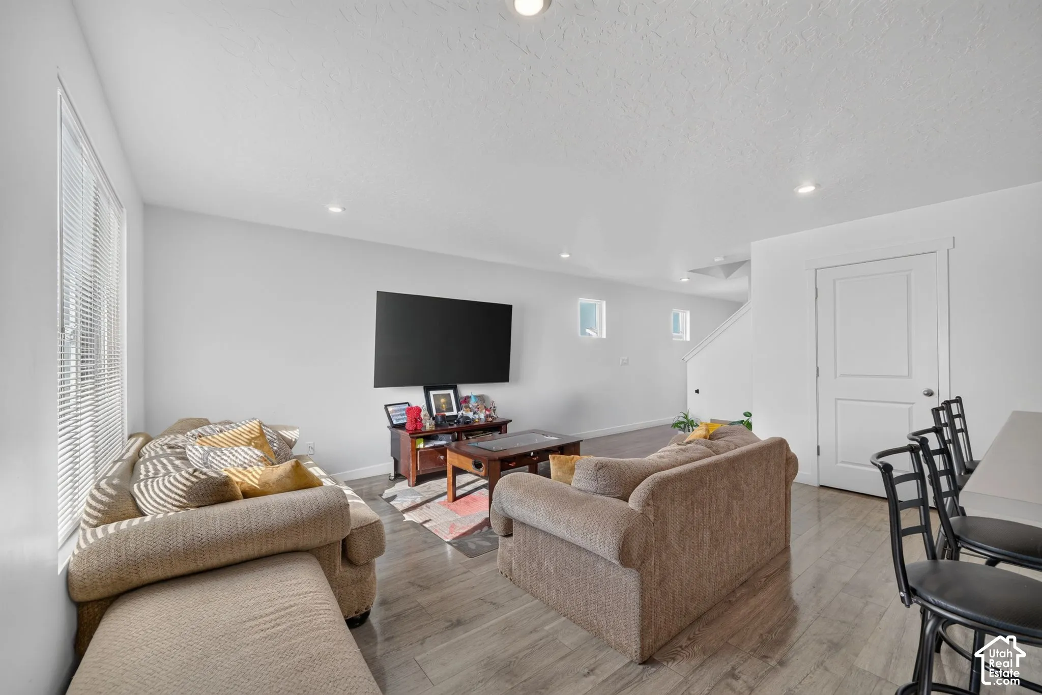 Open-concept space featuring recessed ceiling lighting, wood-finish flooring, two square accent windows, and a white paneled door