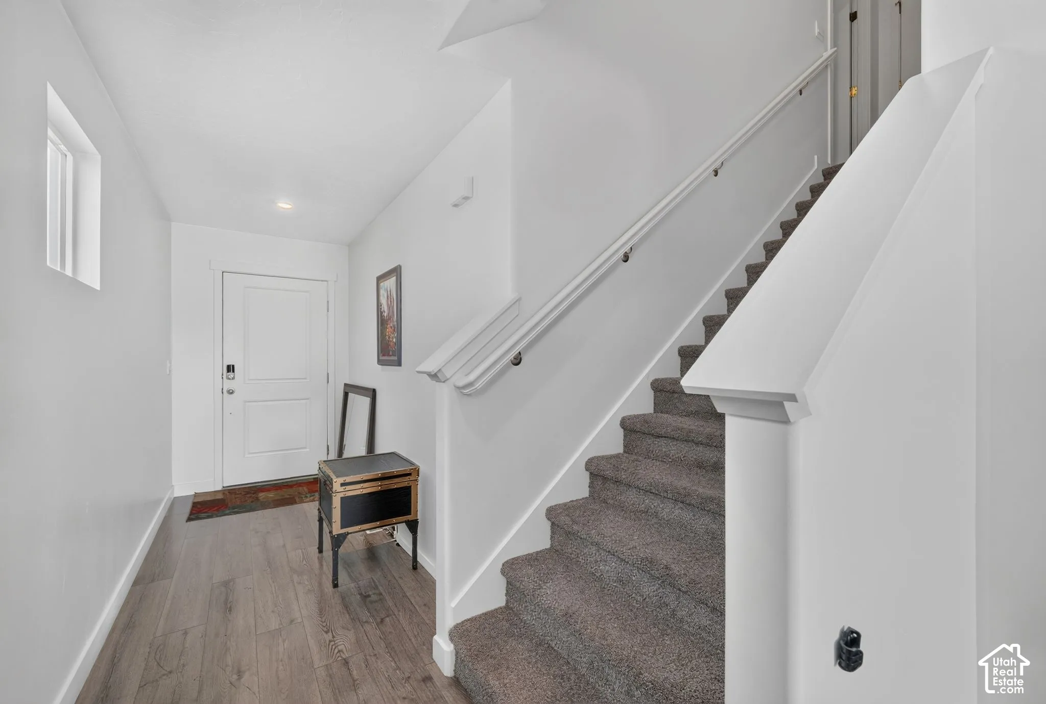 Entryway featuring wood-finish flooring, a paneled door, and a staircase with carpeted treads and a painted handrail
