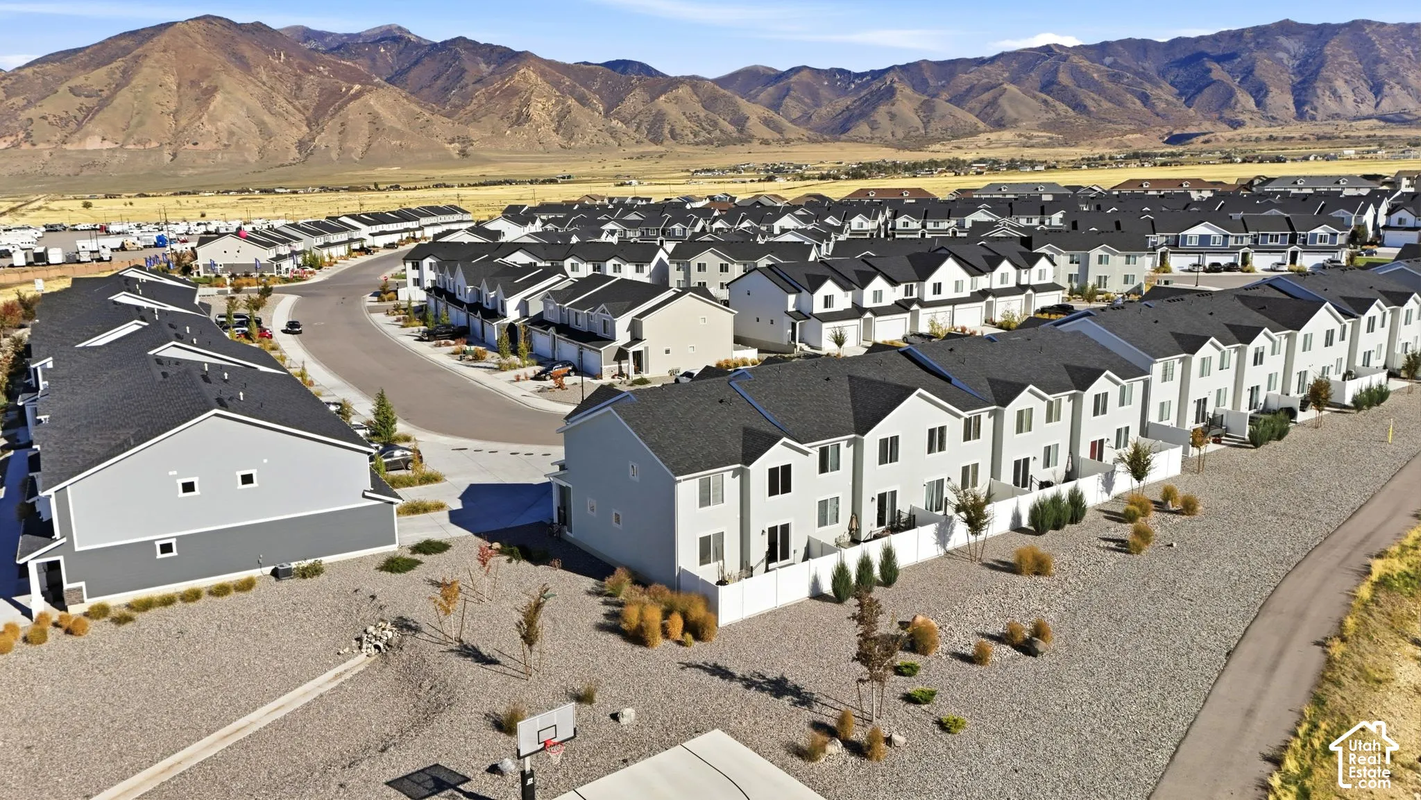 Aerial perspective featuring multi-story residential structures with pitched rooflines, light-toned exterior siding, white privacy fencing, and mountain scenery