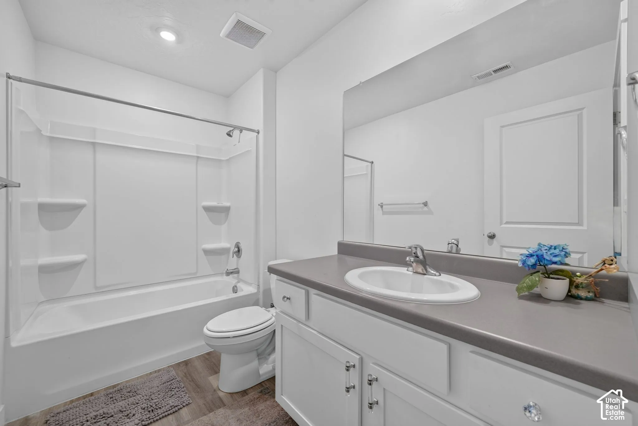 Bathroom featuring white cabinetry, solid-surface countertop, oval undermount sink, full-width vanity mirror, and a combined tub and shower unit