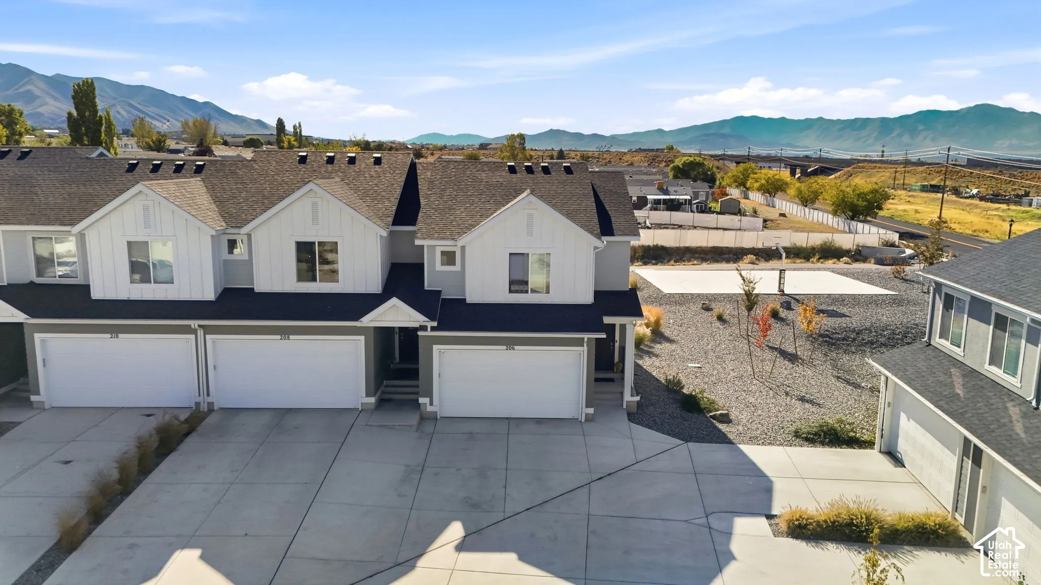 Multi-story townhouse exterior featuring white board-and-batten siding, dual-tone facade, attached multi-car garages, concrete driveways, and mountain scenery