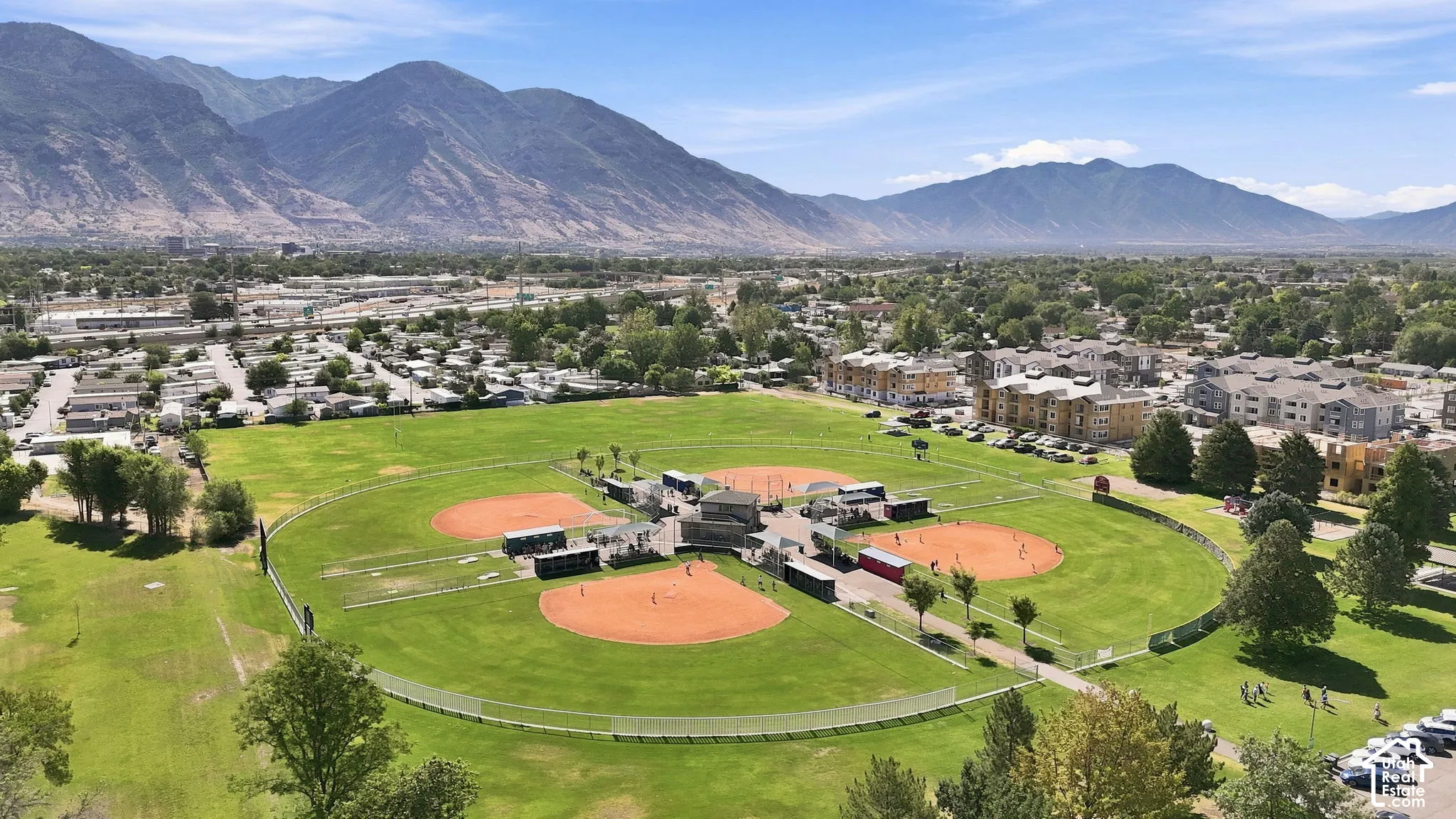 Expansive recreational grounds featuring multiple baseball diamonds, manicured lawns, fenced perimeters, and a mountain backdrop
