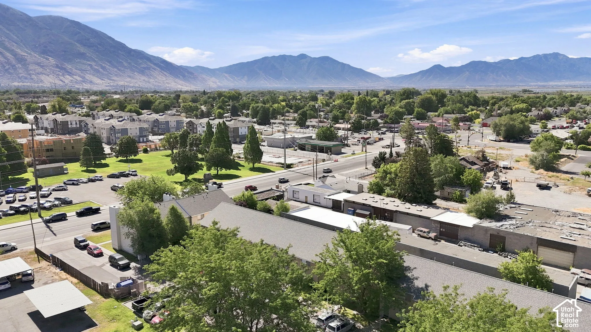 Aerial perspective of the property featuring shingled roofing, paved surface parking areas, and a mountain backdrop