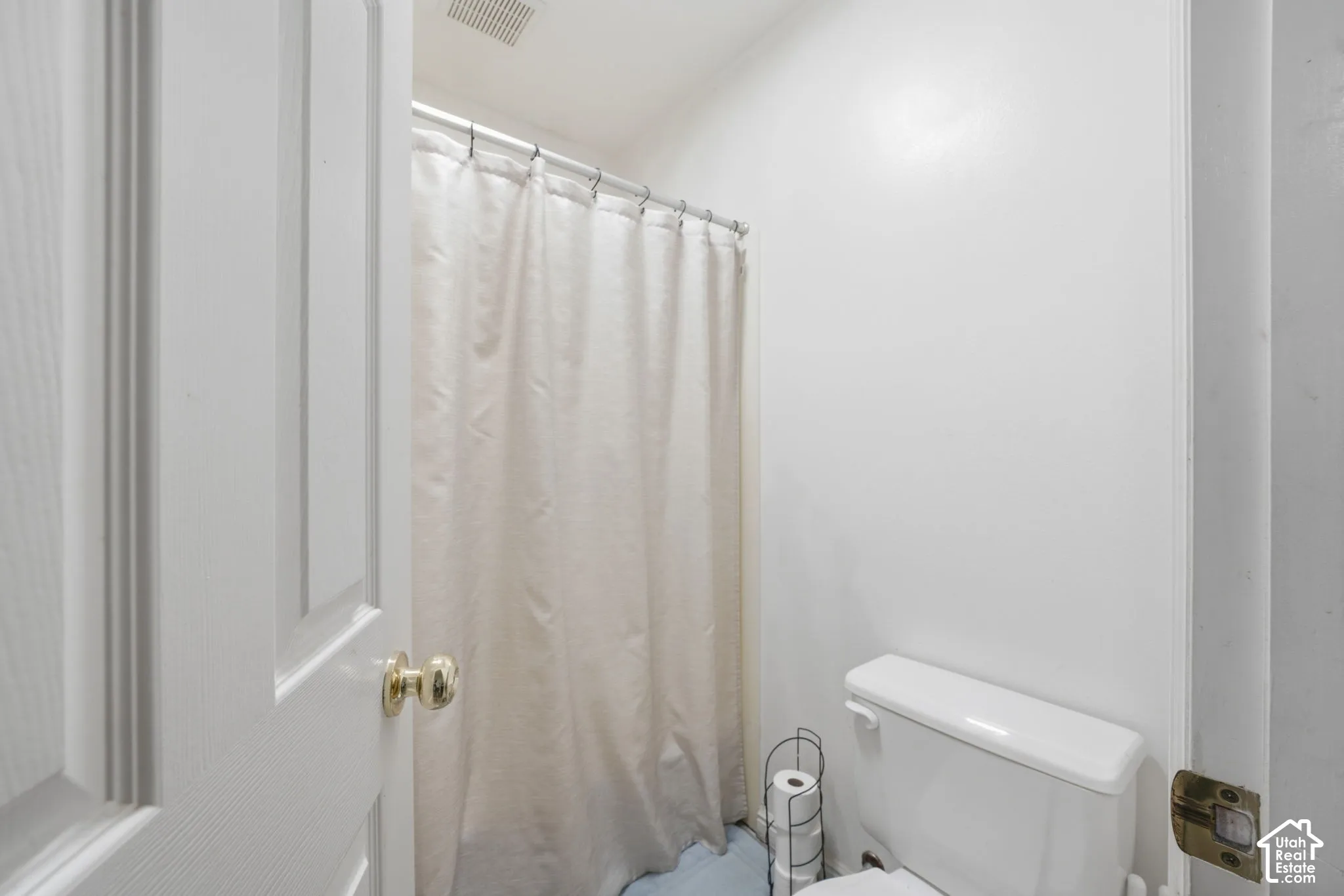 Full bathroom featuring a shower-tub combination with a curtain rod, porcelain toilet, and a paneled door with polished brass hardware
